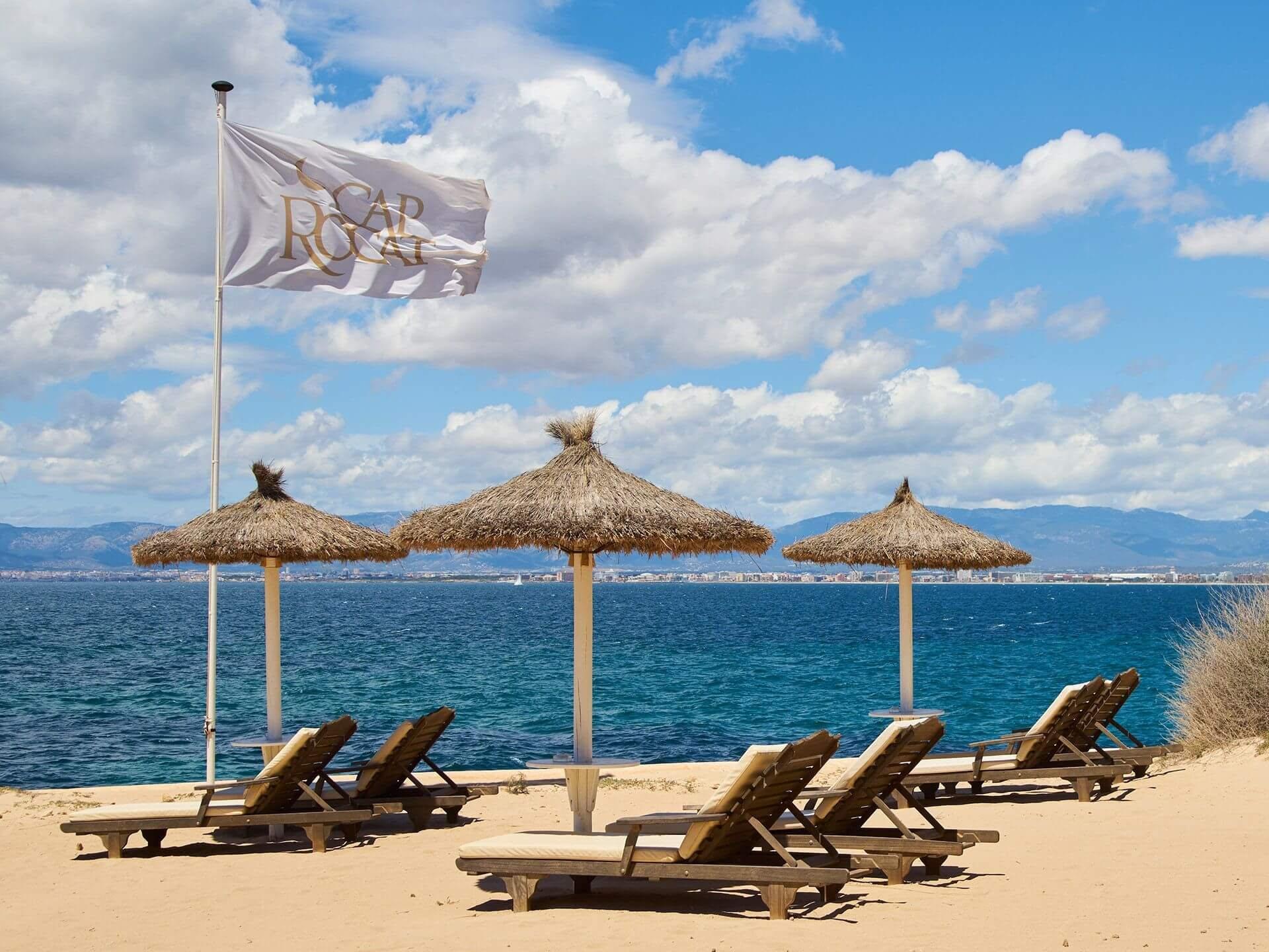 Cap Rocat: a private beach cove with thatched umbrellas and loungers on sand beneath clear skies