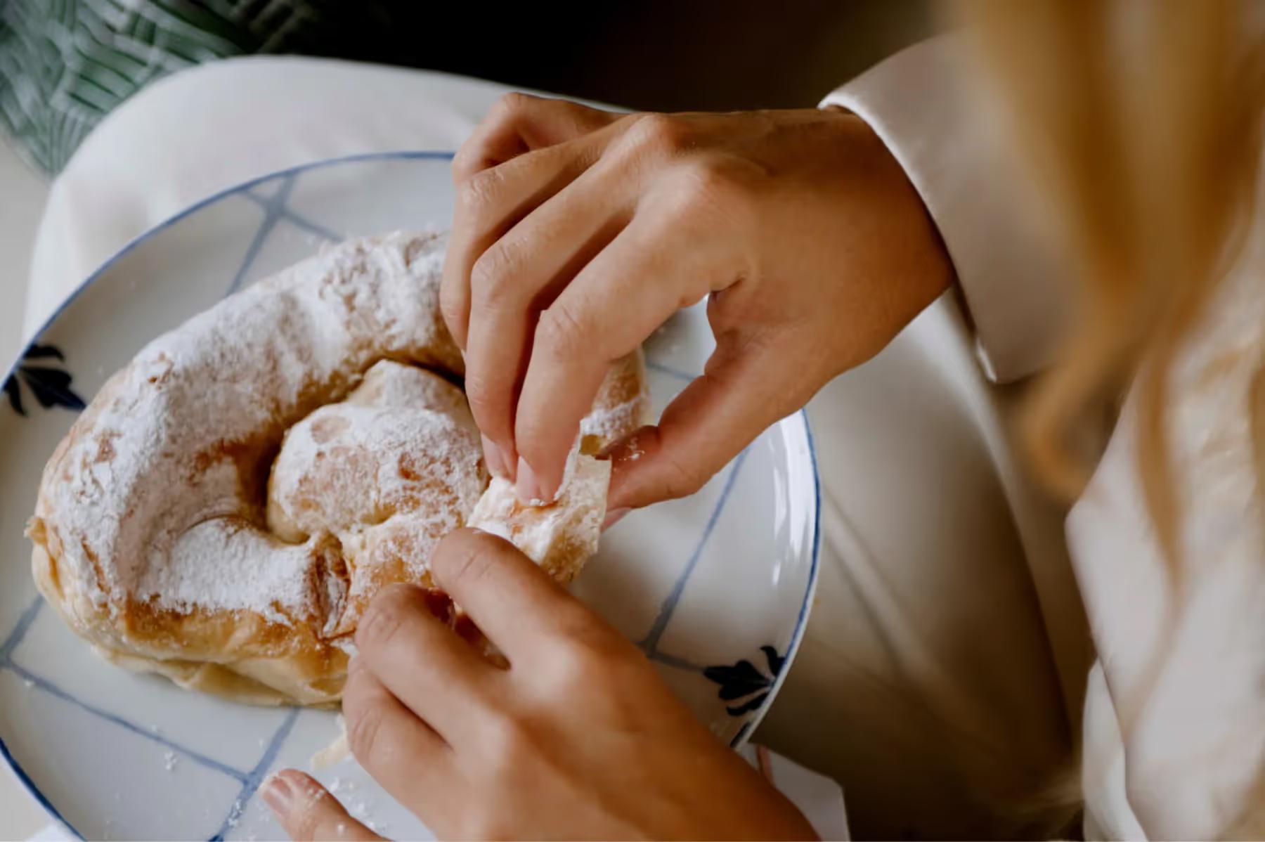 Hands breaking artisan bread over a white plate during meal