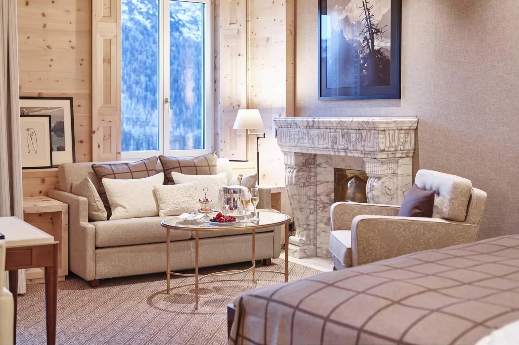 Kulm Hotel St. Moritz: a suite with a sofa and fireplace, framing a snowy Alpine landscape