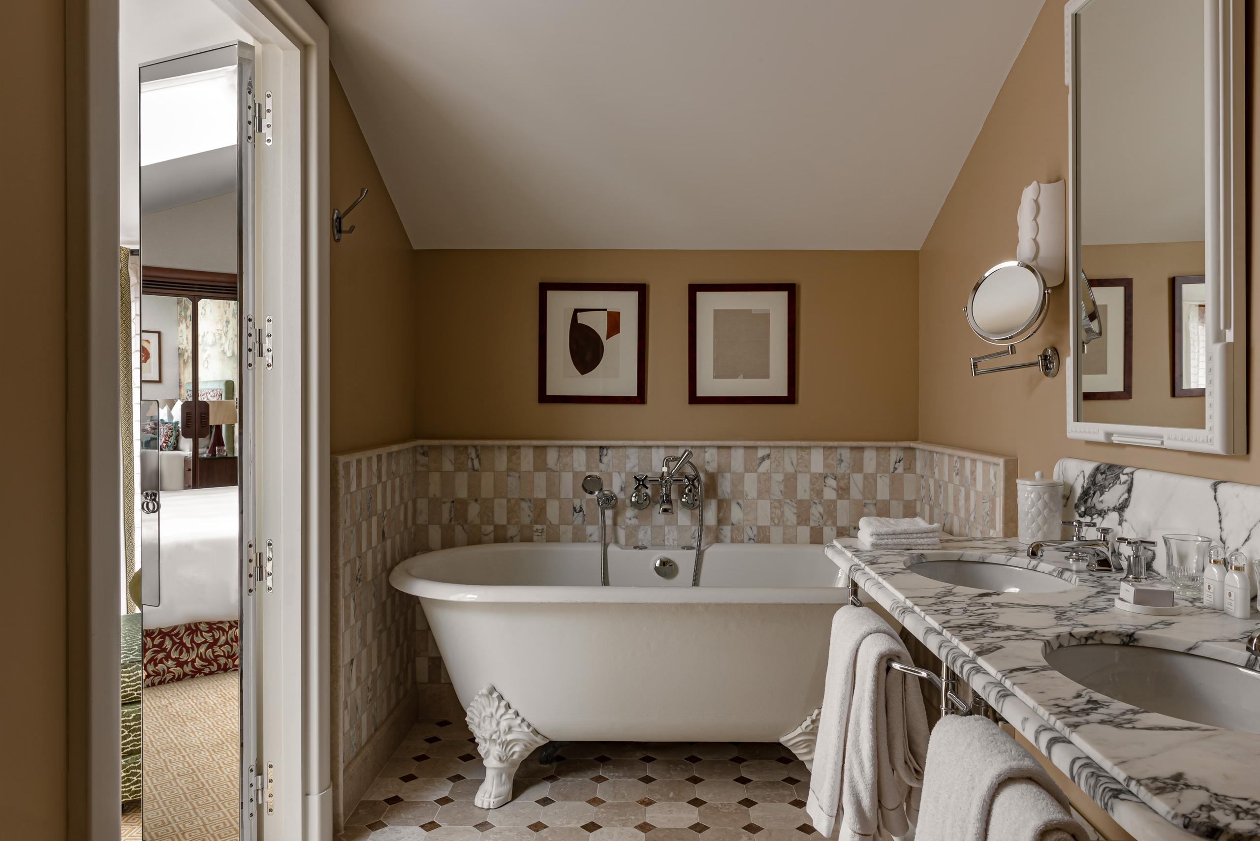 Saint James: spa bathroom with white free-standing tub, marble details, and window overlooking garden