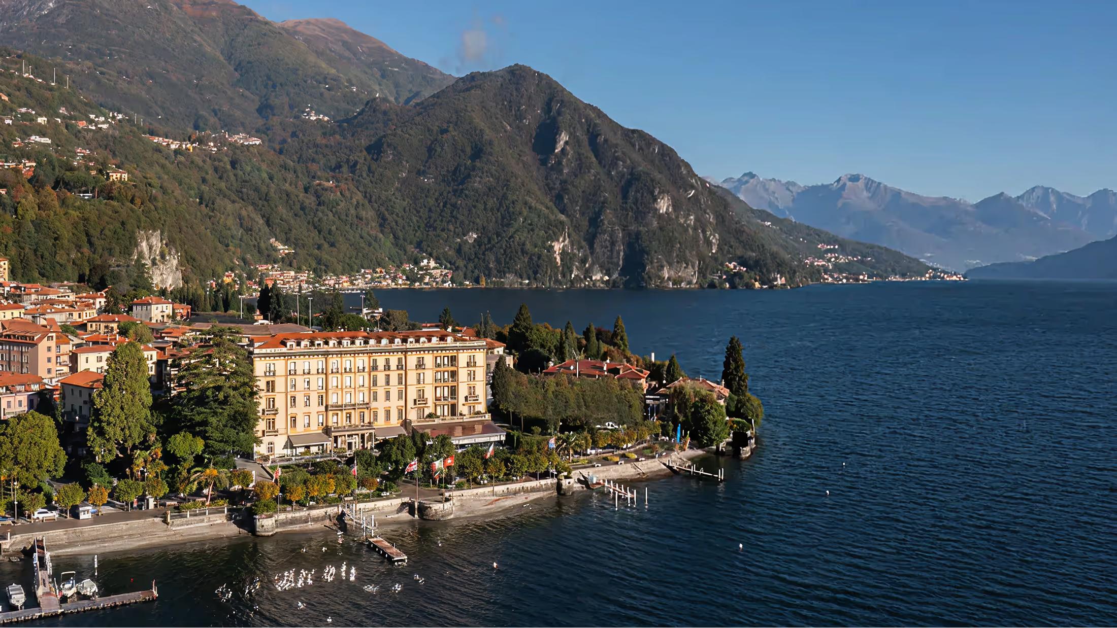 A lakeside hotel with golden-beige facades overlooking blue water and mountains