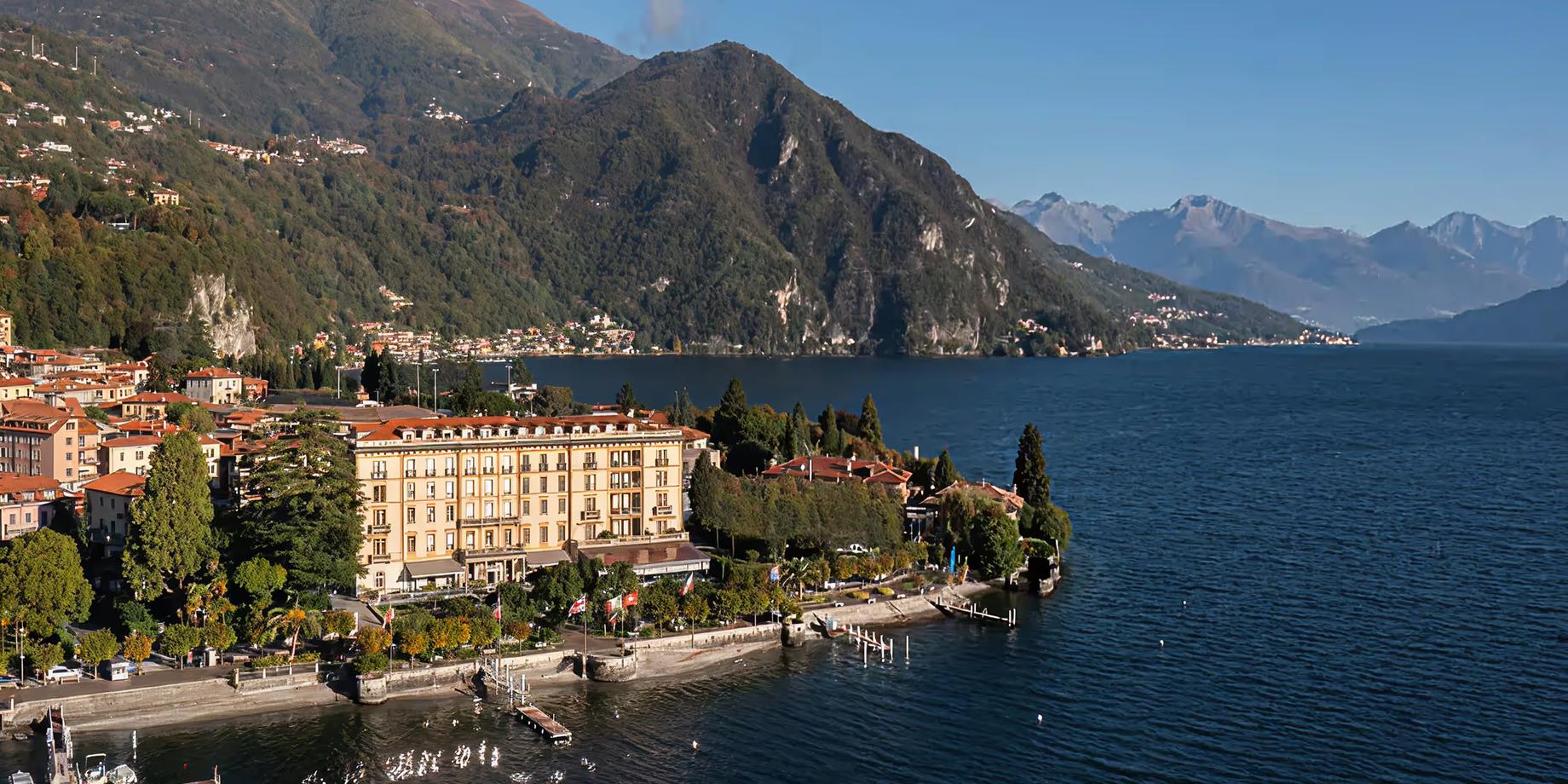 A lakeside hotel with golden-beige facades overlooking blue water and mountains