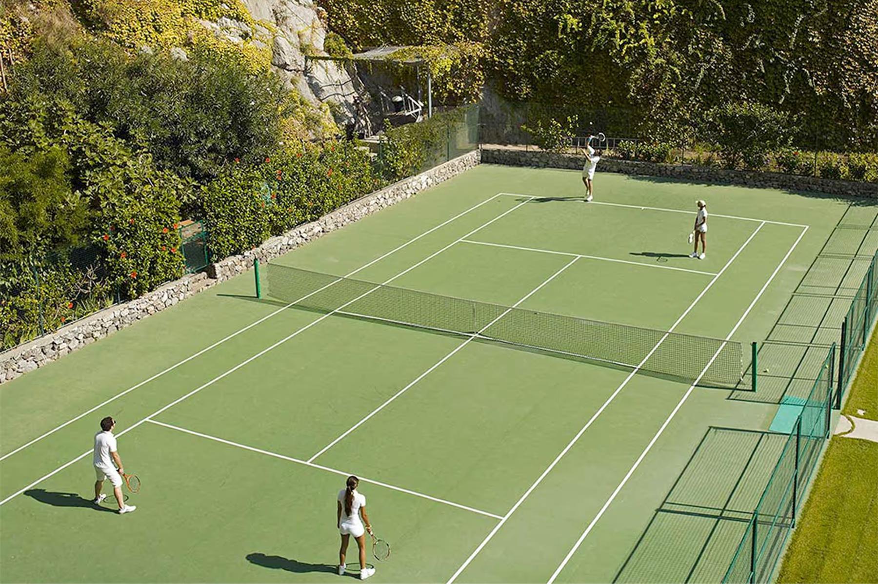 Tennis court at cliff edge with players, net, and panoramic sea and coastline views