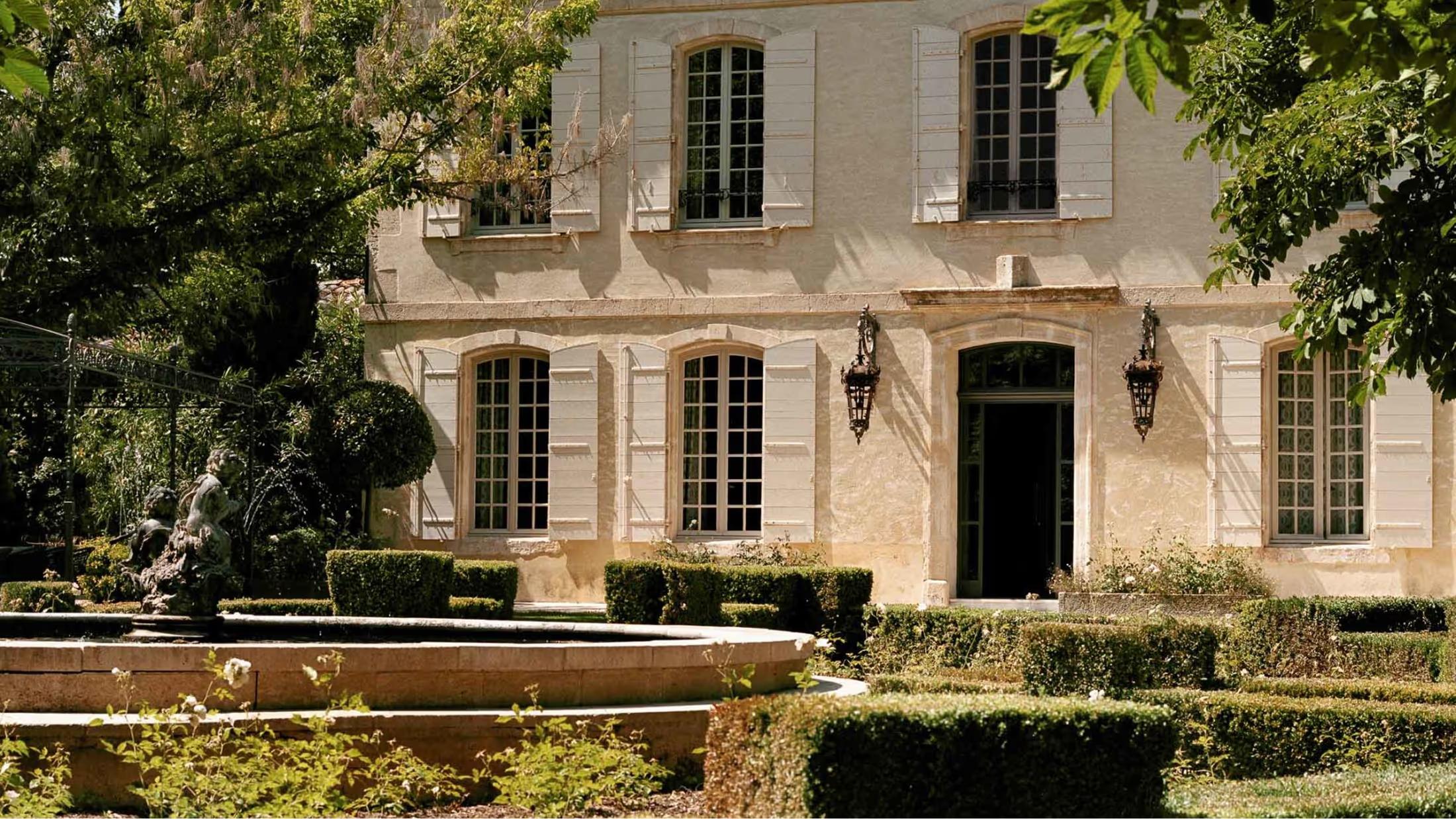 Stone estate facade with dark shuttered windows and manicured landscape