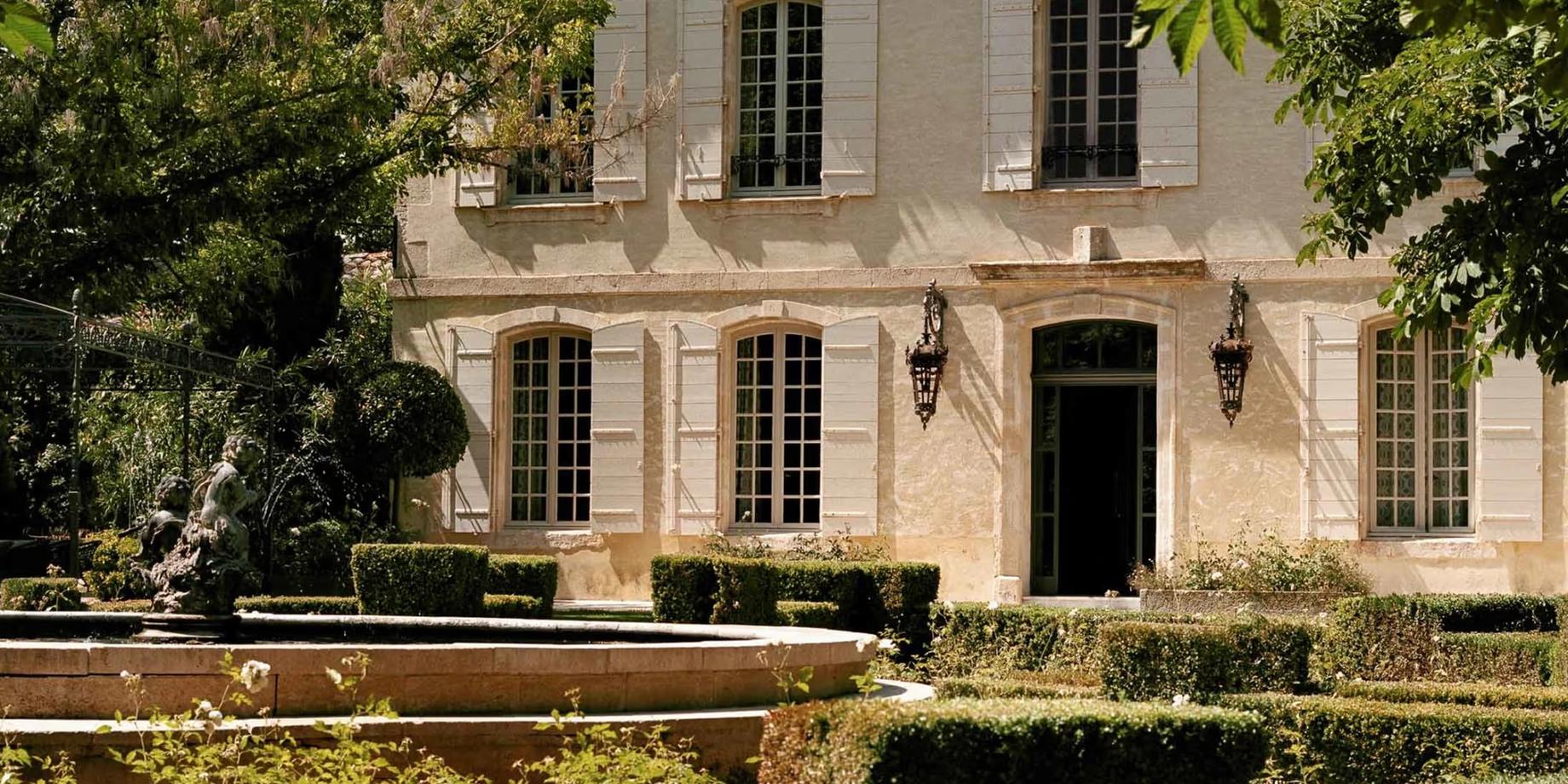 Stone estate facade with dark shuttered windows and manicured landscape