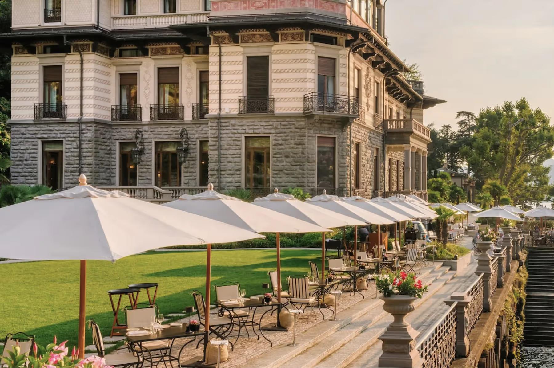 Stone terrace with white dining umbrellas, traditional villa architecture, and manicured lawn