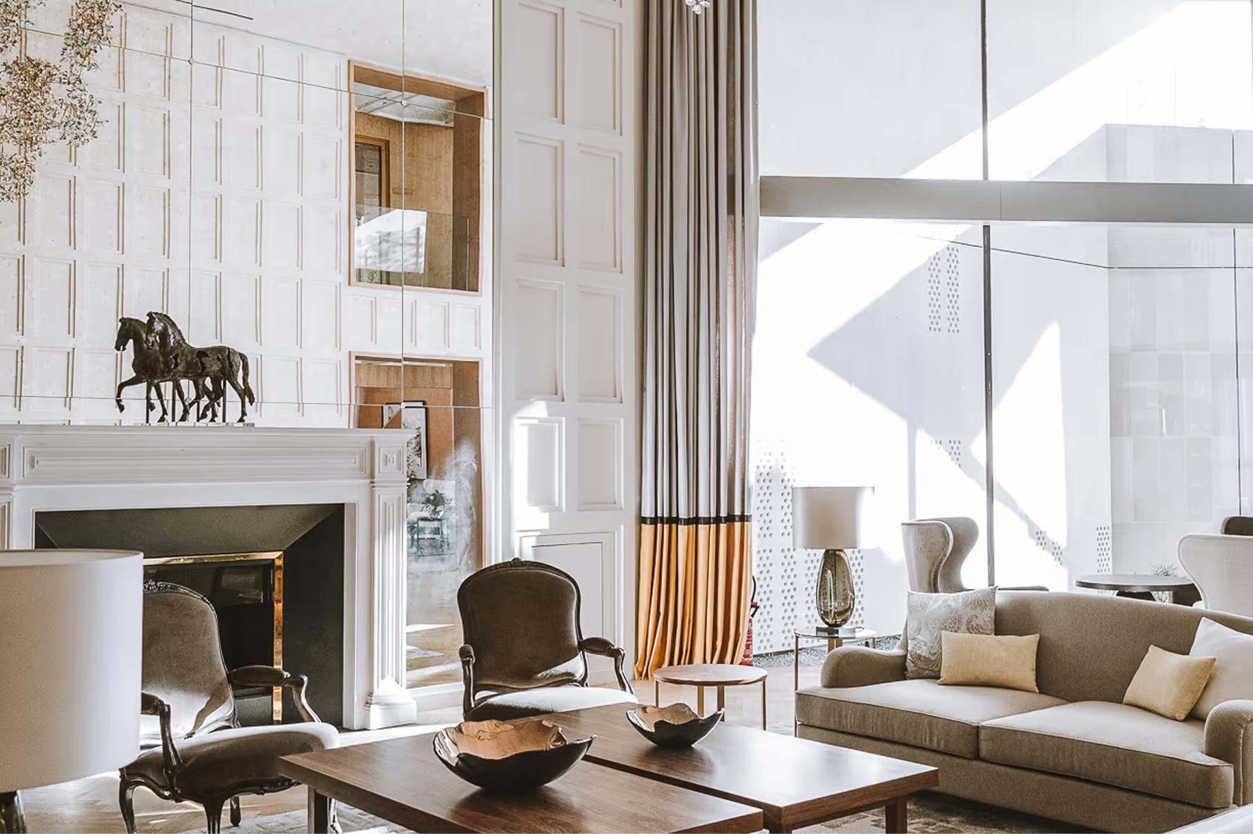 Modern lounge with high ceilings, fireplace, dark seating, and bright architectural sunlight
