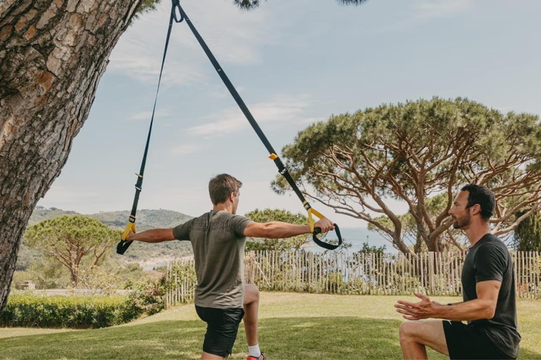 Lily of the Valley: two people doing suspension training exercises under large tree