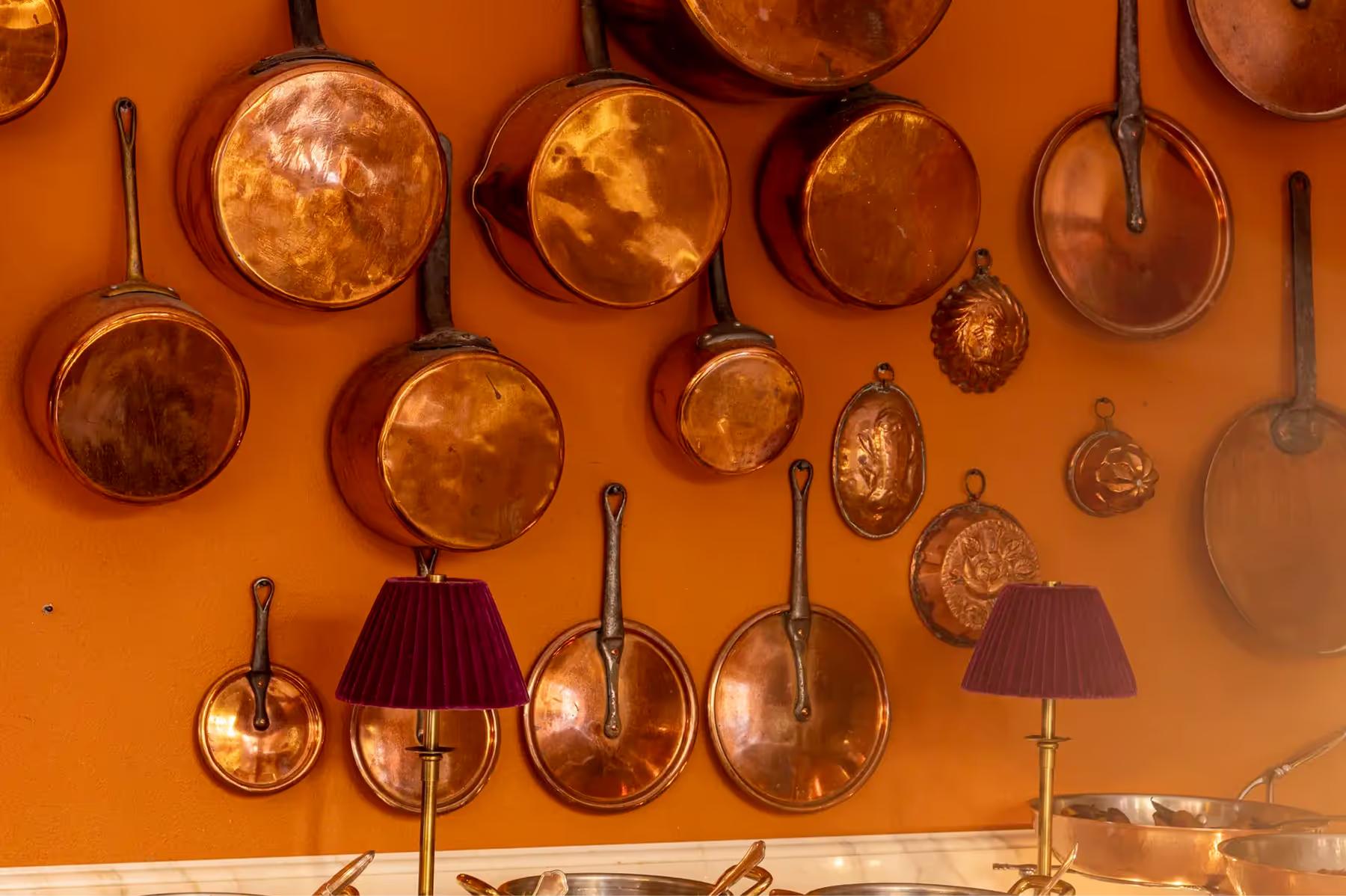 Hanging copper pots and pans displayed on a burnt-orange accent wall
