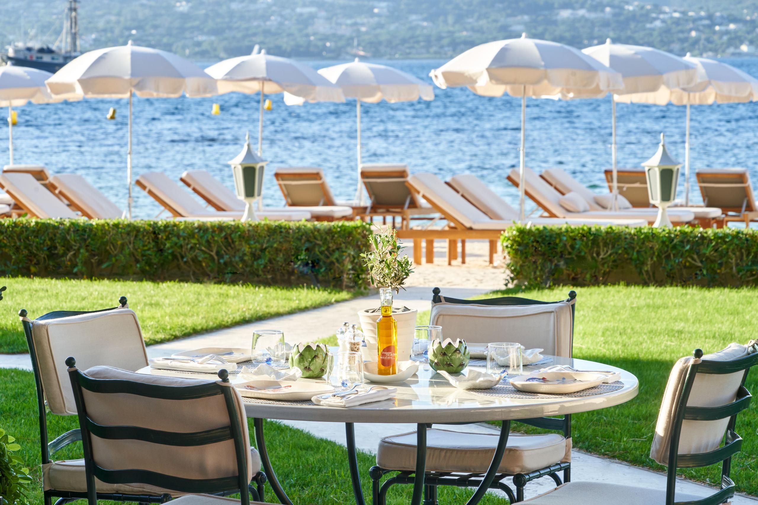 Cheval Blanc St-Tropez: grass terrace with round table and striped umbrellas overlooking bay