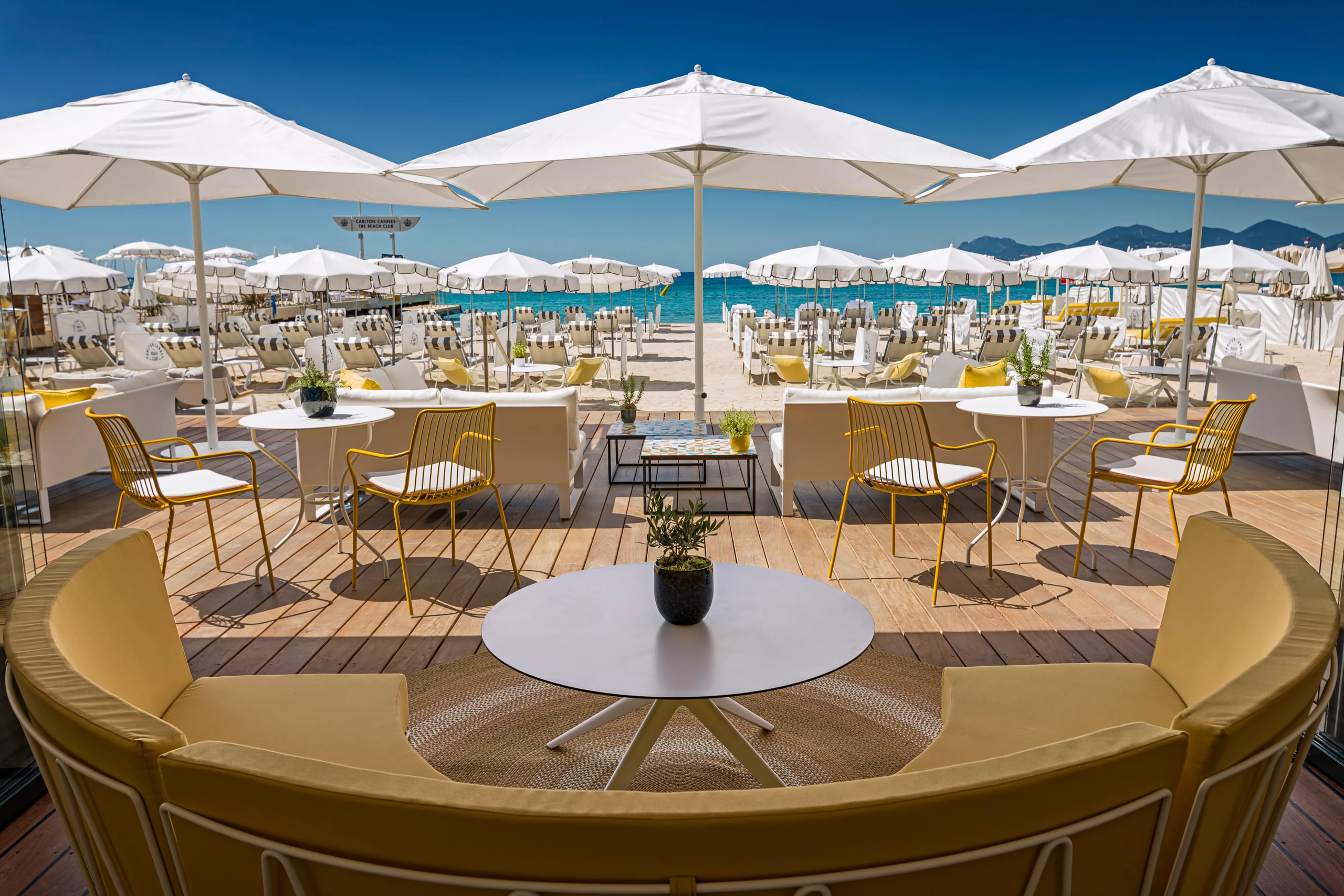 Beach club seating area with round tables under white umbrellas and clear blue sky above