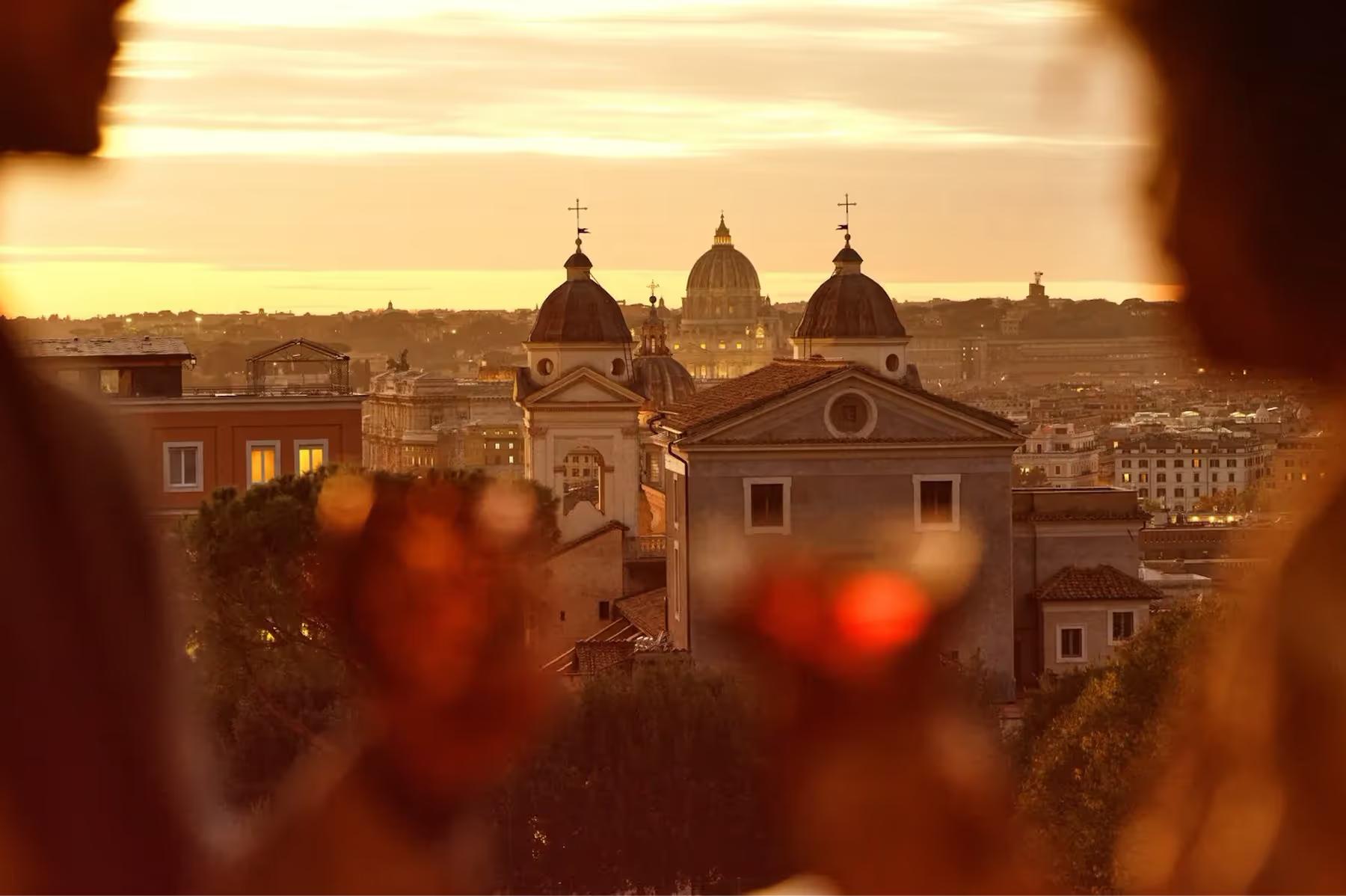 Hotel Eden: a view through ornate red glass vessels to Rome’s domes and architecture at golden hour