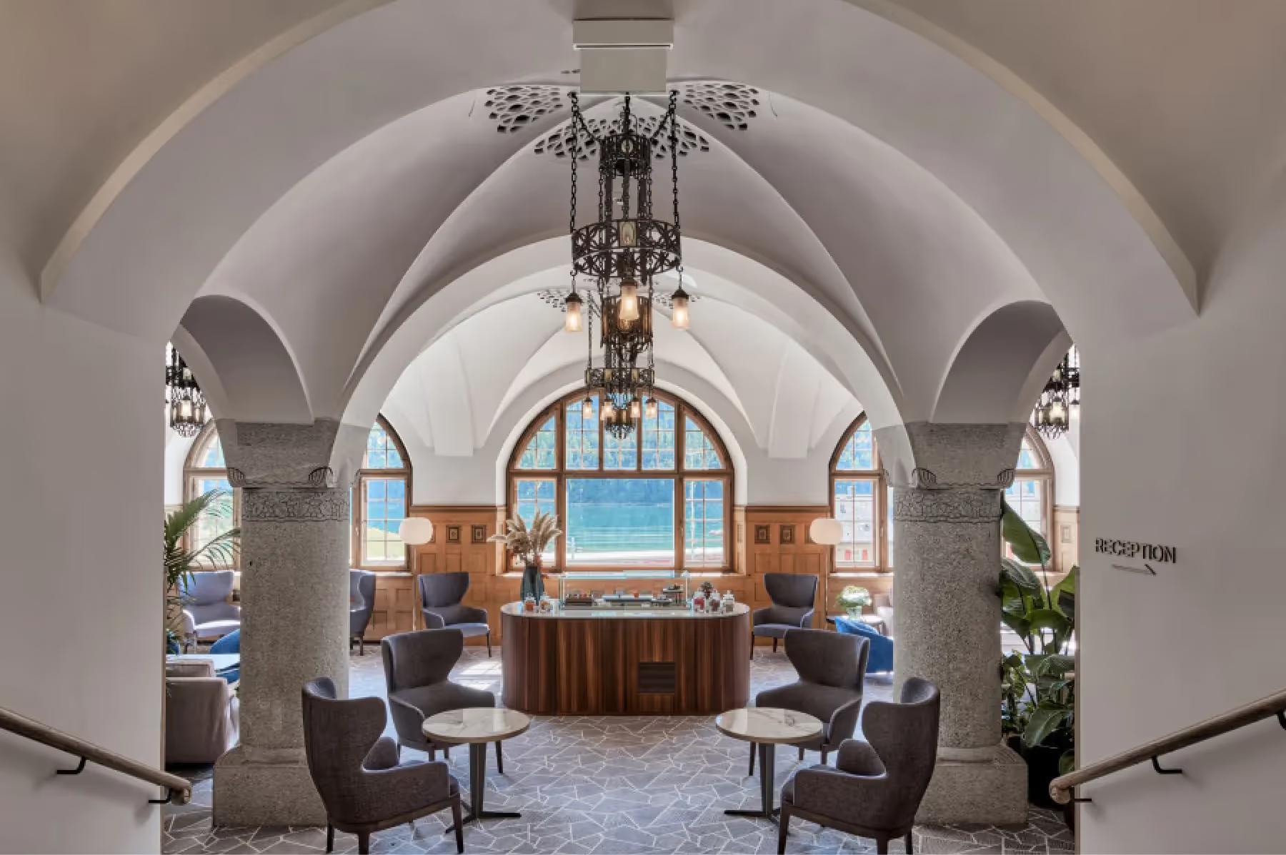 Grace La Margna St. Moritz: grand arched hallway with ornate chandeliers, blue window alcoves, and fireplace