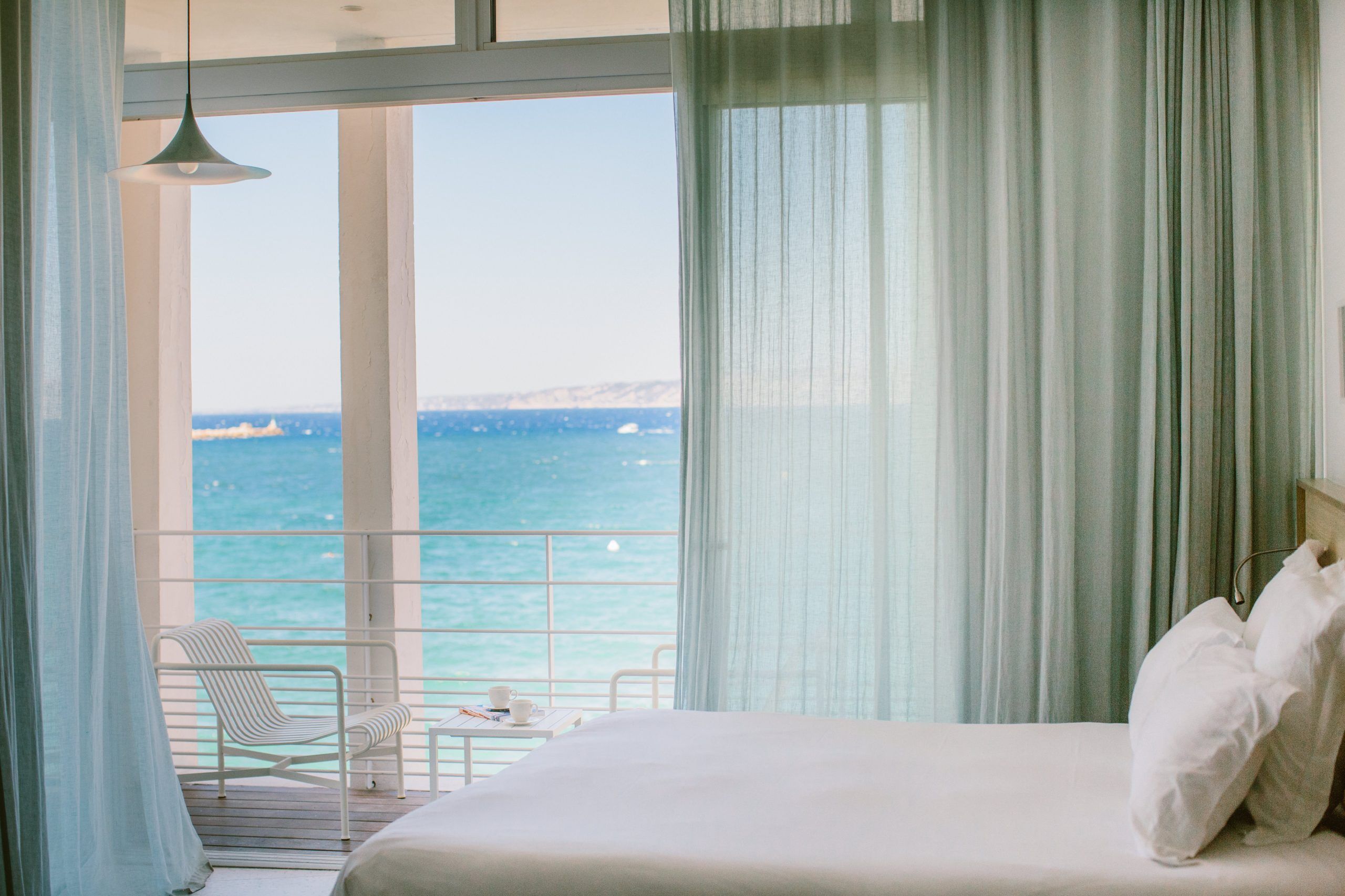 A junior suite at Les Bords de Mer in Marseille, the bed facing pale curtains and a window open onto the sea