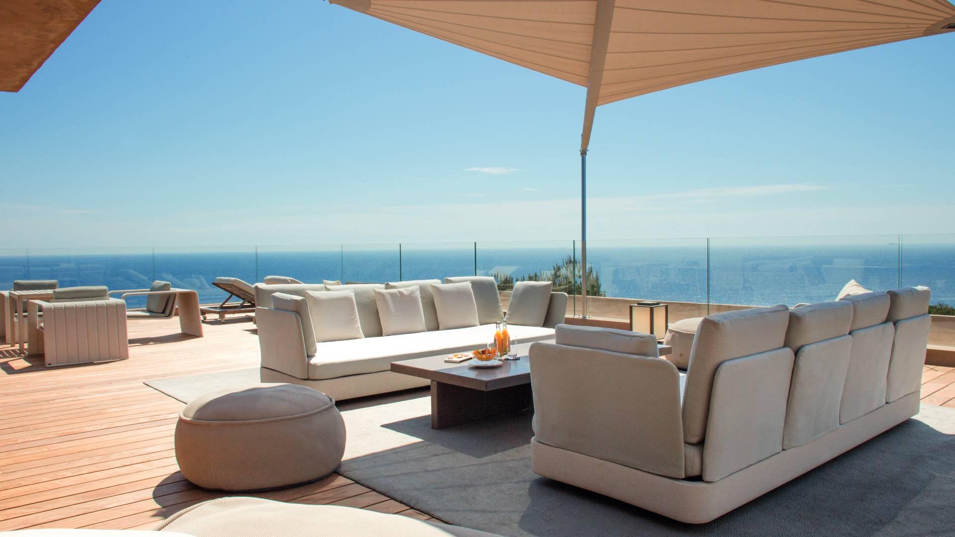 La Réserve Ramatuelle: oceanside terrace with cream sofa and wooden umbrella in sunlight