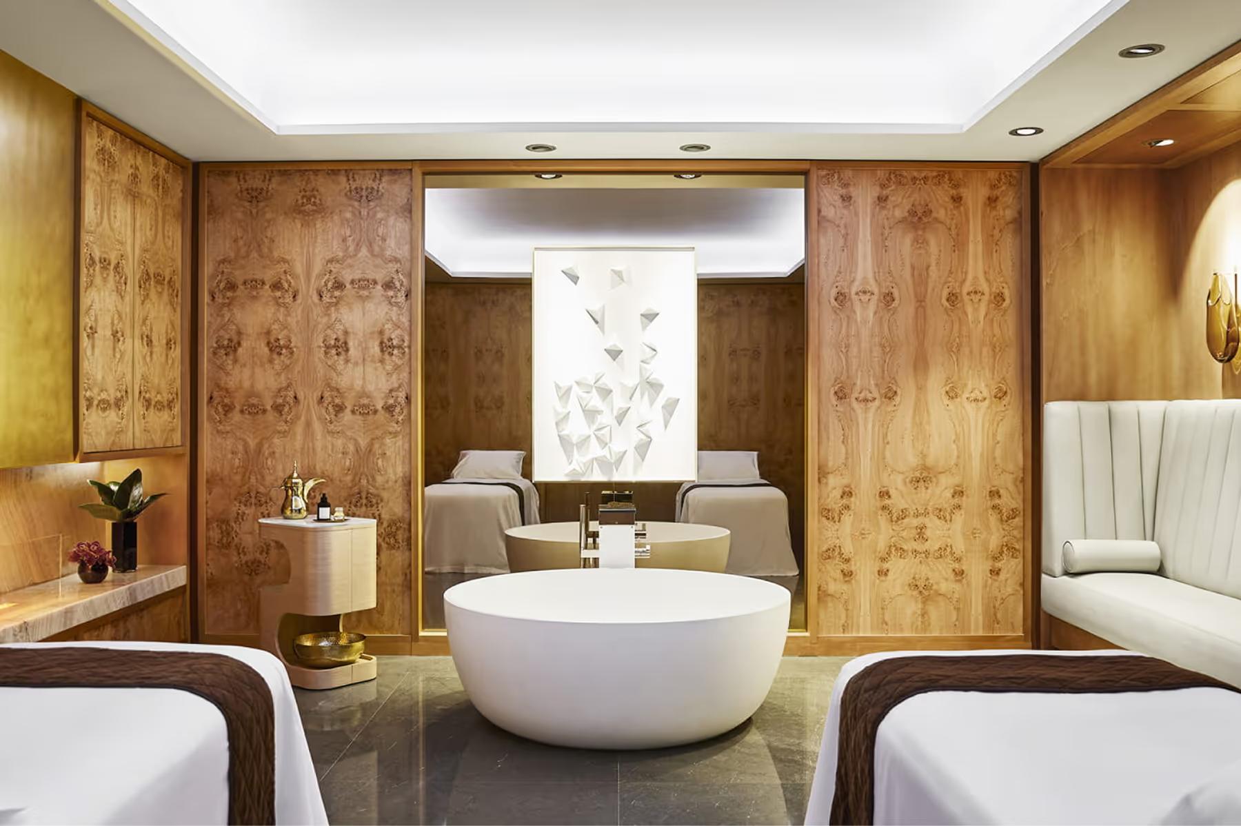 Four Seasons Hotel Madrid: spa treatment room with round marble tub, warm wood paneling, and cream leather seating