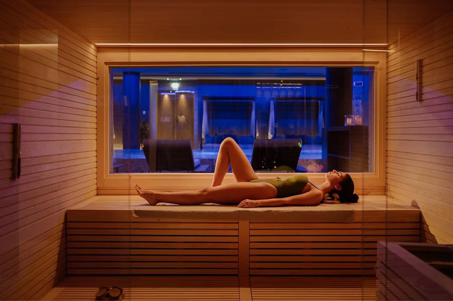A spa room with a woman in a plunge pool surrounded by wood and blue light