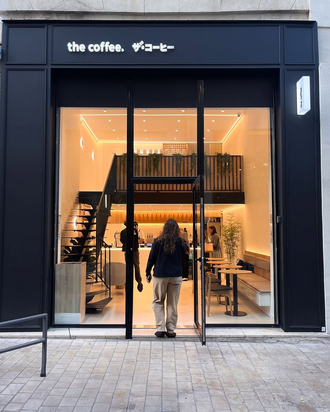 The black shopfront of The Coffee on Rue Haxo, open onto a warmly lit room with a mezzanine above the counter