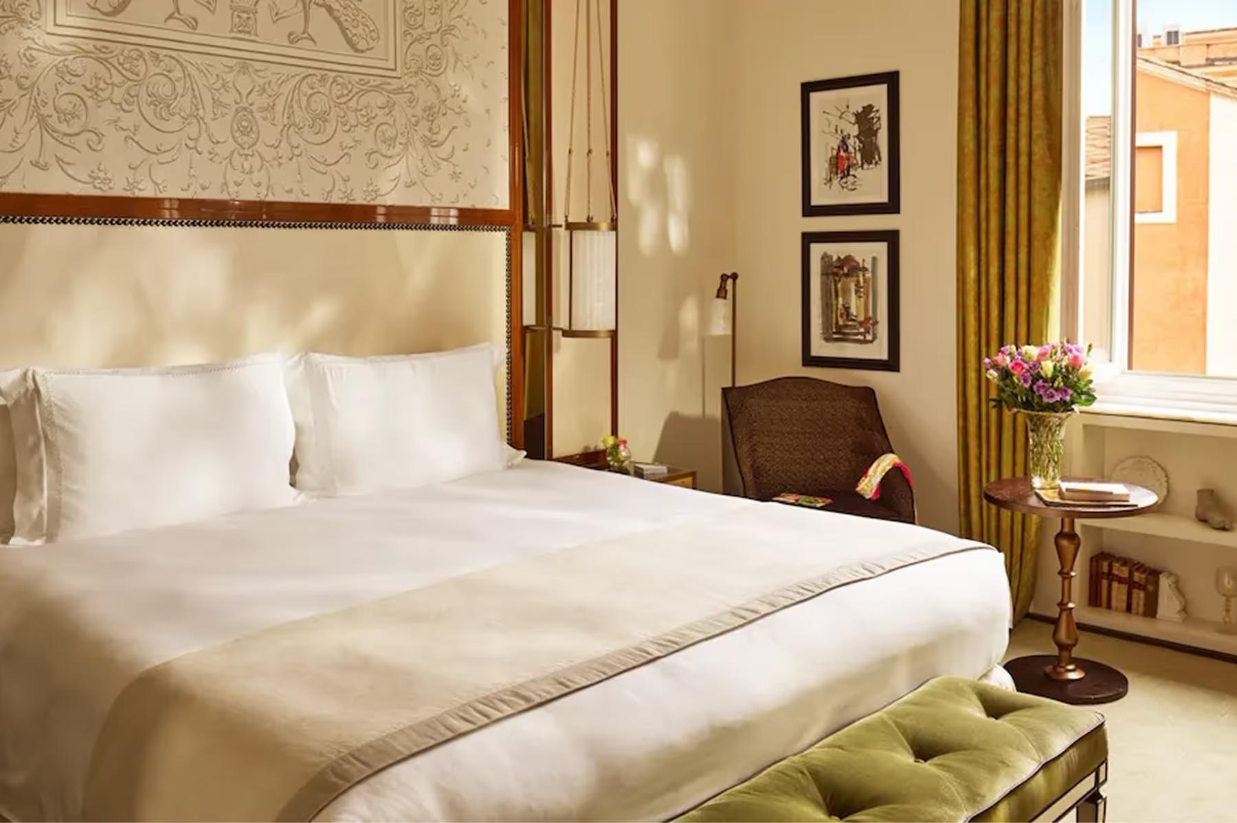 A bedroom with a canopy bed, taupe headboard, window with gold curtains, and dark wood nightstands