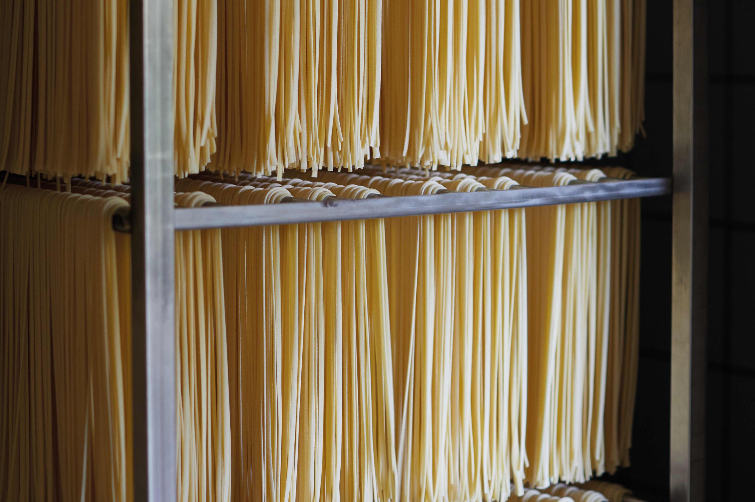 Caruso: fresh homemade pasta nests arranged on wooden shelves for cooking classes