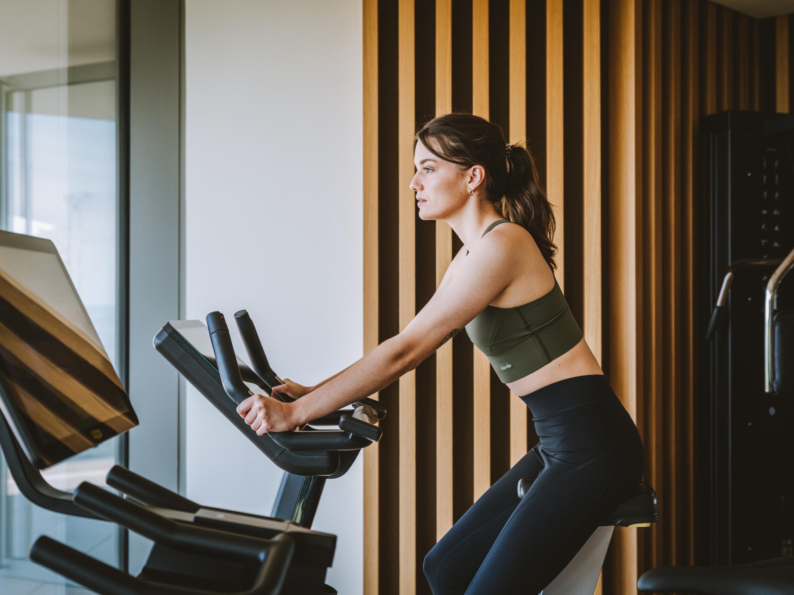 Royal Champagne Hotel & Spa: woman on exercise bike in fitness room with striped accent wall and natural lighting