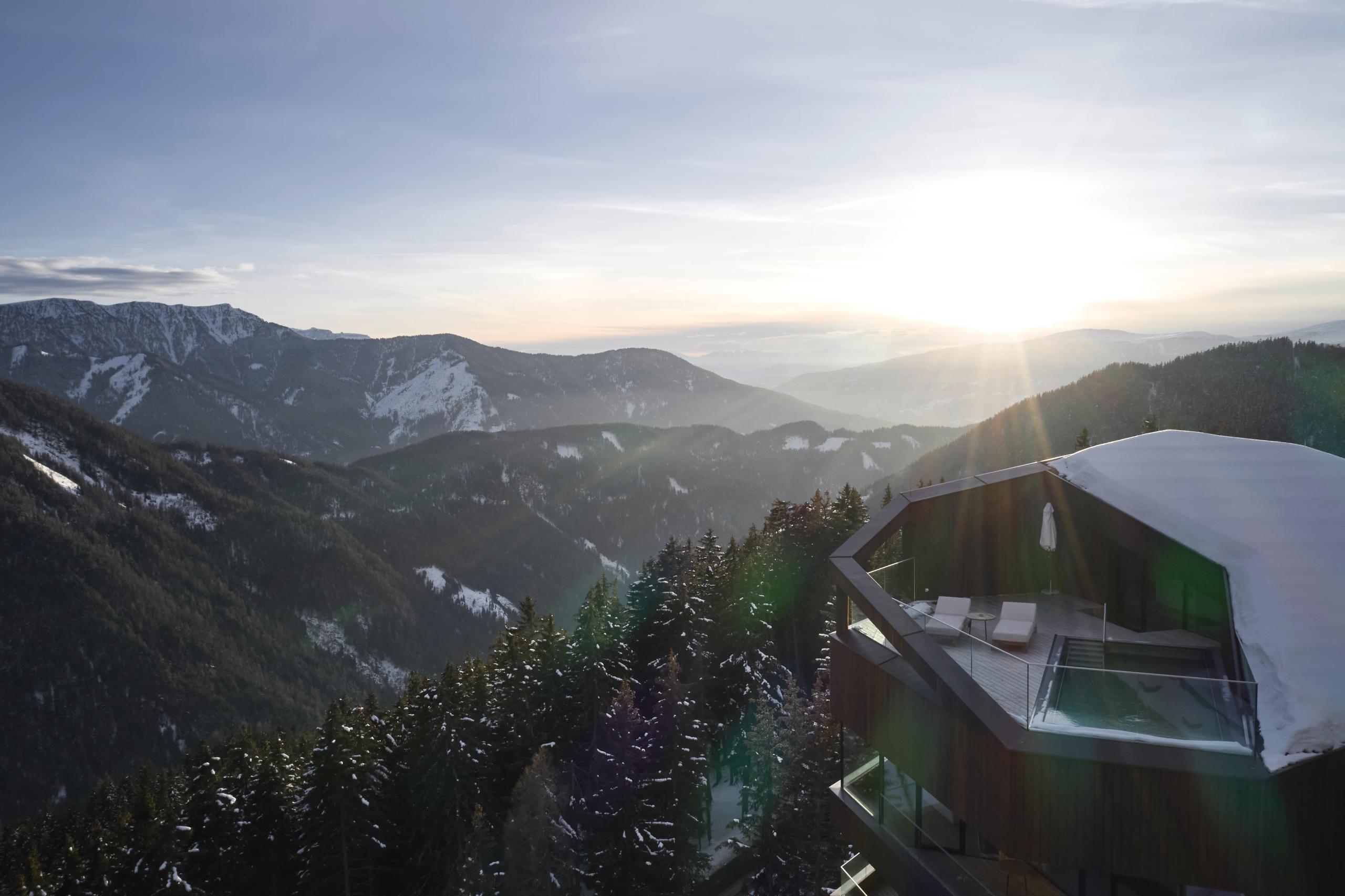 Forestis: an aerial view of the building’s modern architecture set in mountains at sunset with forested slopes