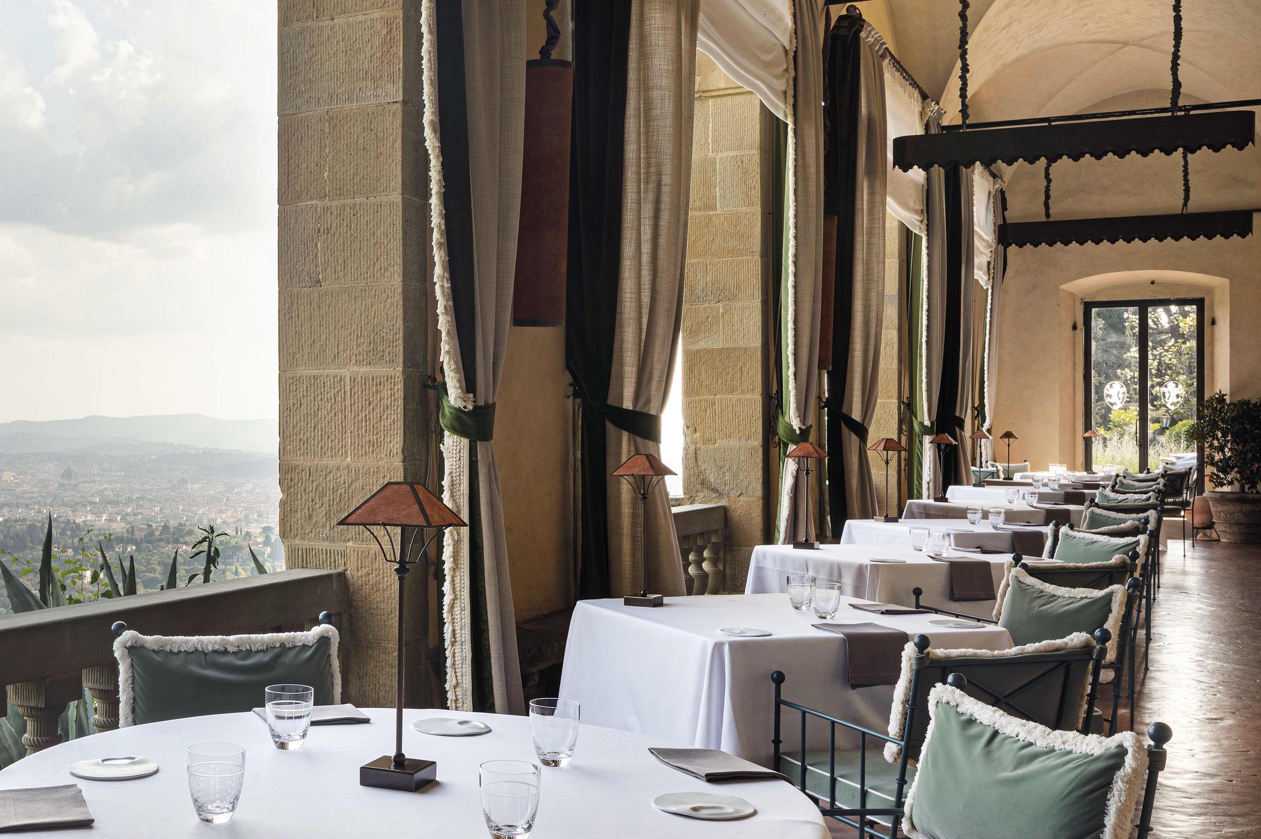 Villa San Michele: a formal dining room with tall columns, white tablecloths, and sweeping views to distant hills