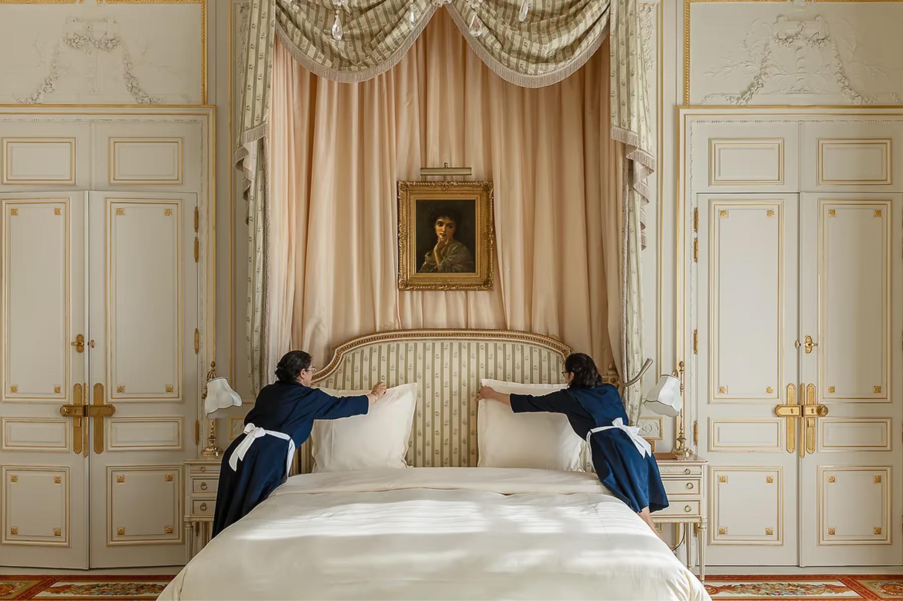 A bedroom with cream paneled doors, draped bed canopy, and classical gilt detailing