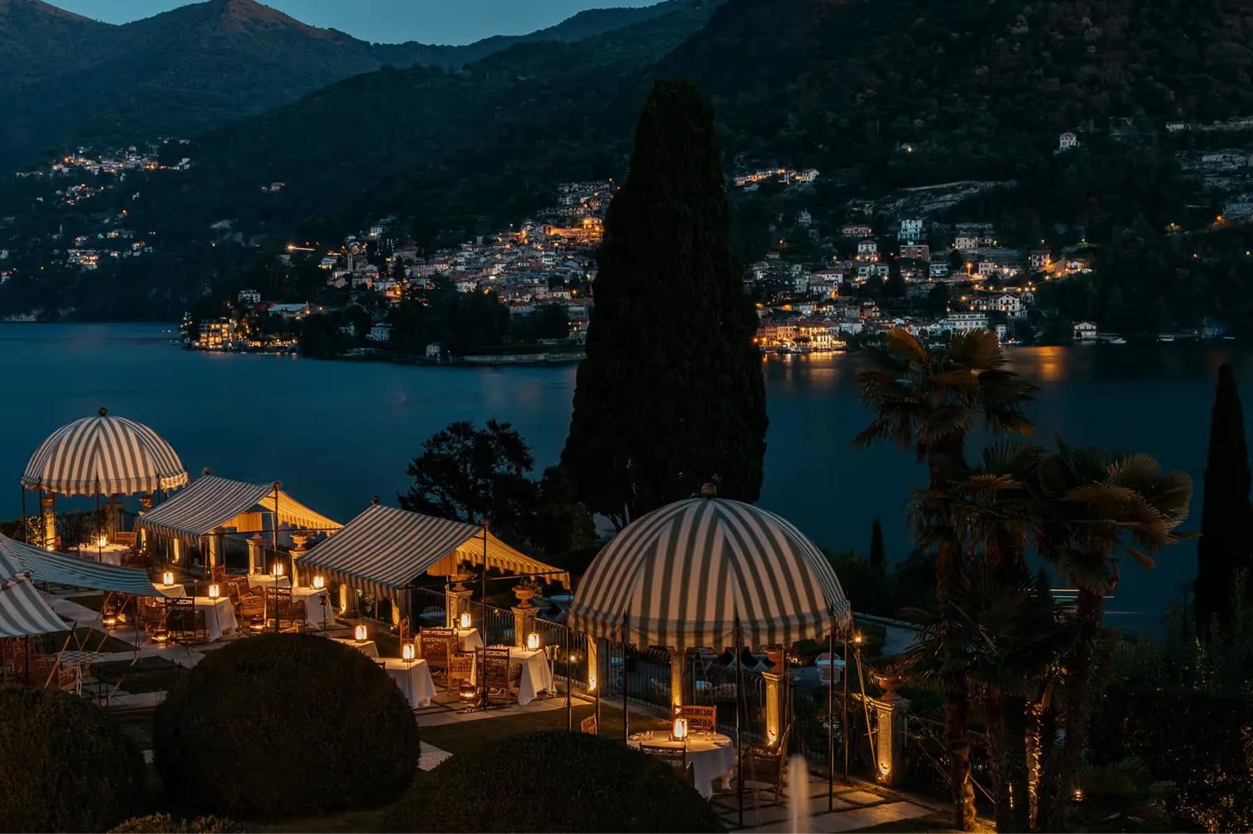 Passalacqua: outdoor terrace at dusk with illuminated dome tents, lake town lights below