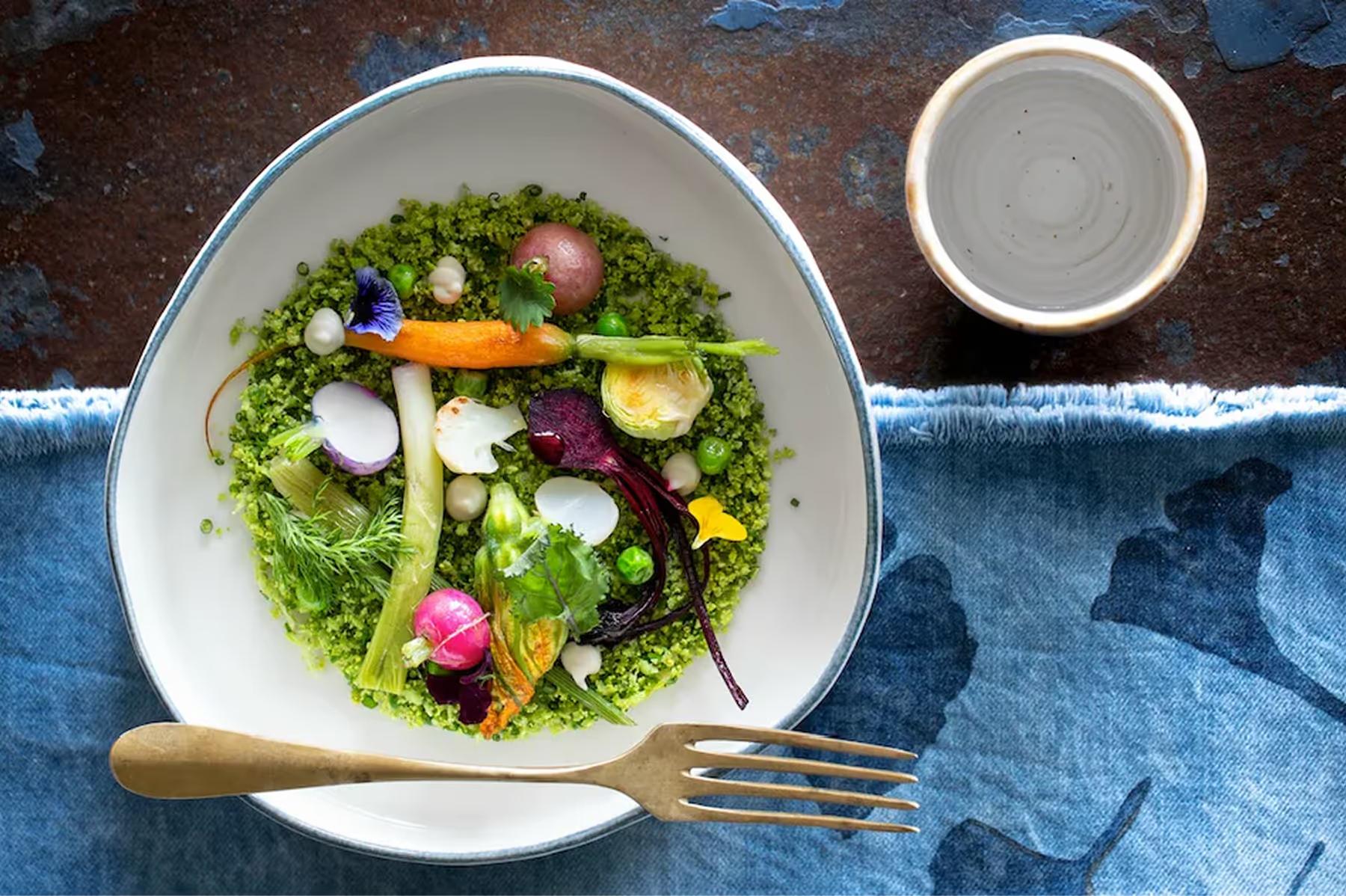 Chenot Palace Weggis: wellness cuisine plated in white bowl: mixed greens with vegetables and edible flowers on blue tablecloth