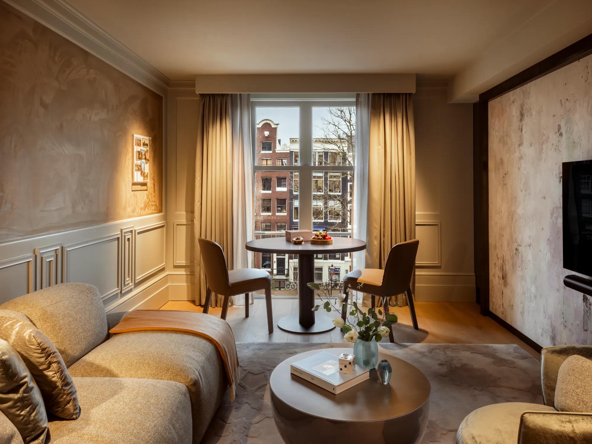 Rosewood Amsterdam: the Canal View Executive Suite living room with a sofa and a dining table by the window