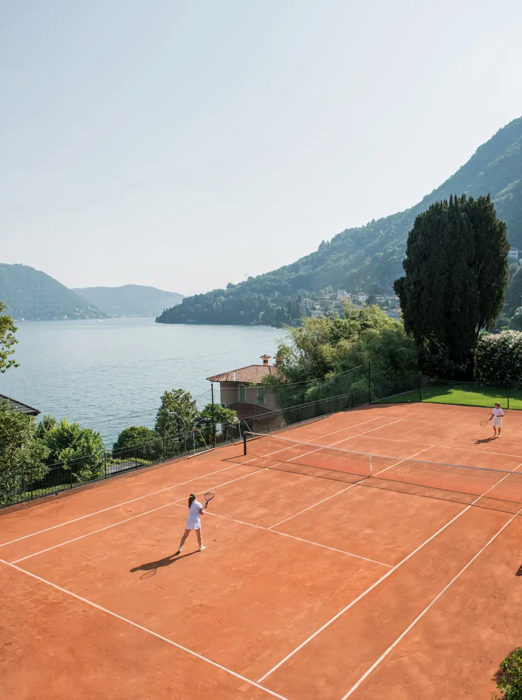 A red clay court on the lowest garden terrace at Passalacqua, Lake Como beyond