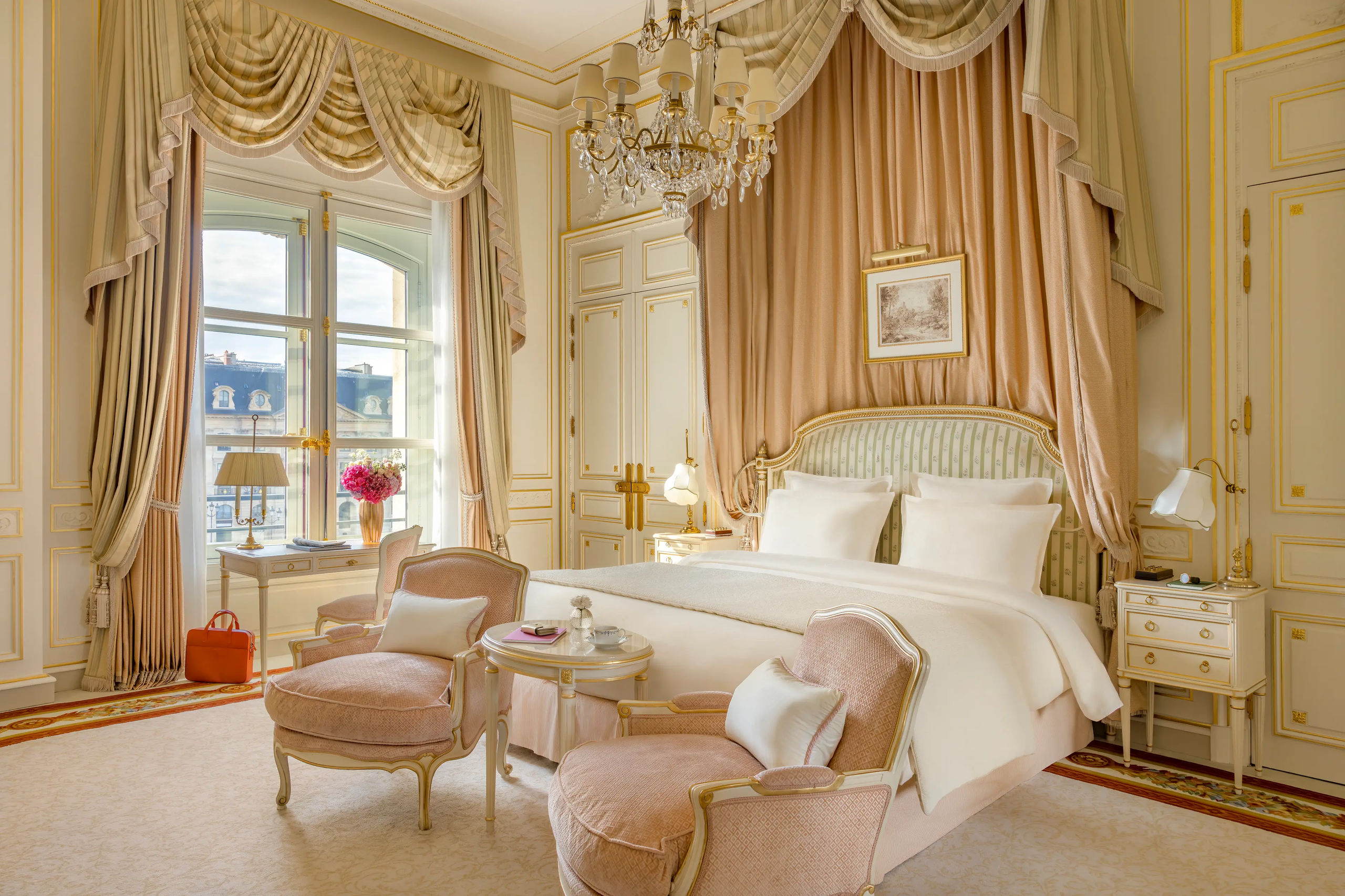 A bedroom with gilt curtain rods, gold drapery swags, cream upholstered seating, and polished hardwood floor