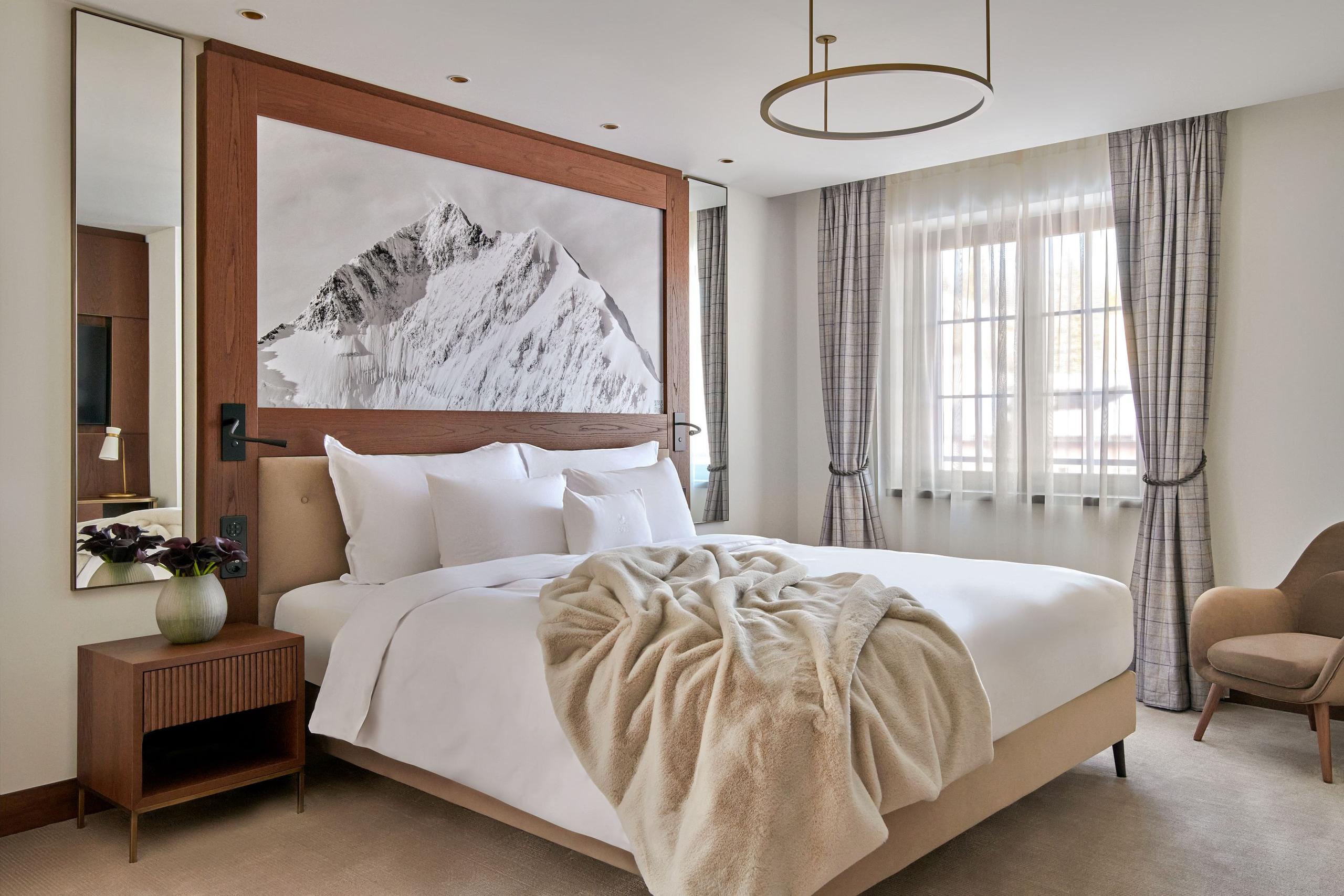 Grace La Margna St. Moritz: suite bedroom with wood headboard, cream bedding, and artwork above alpine views