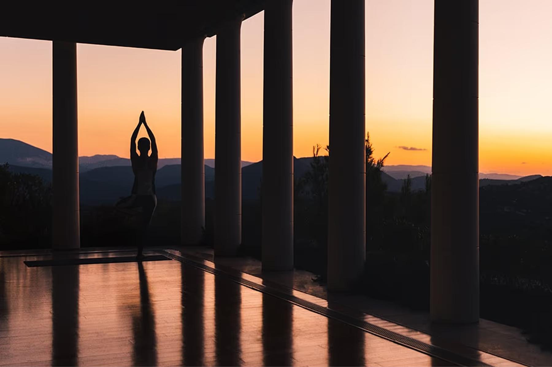 Amanzoe: person in yoga pose at sunset with columned structure framing