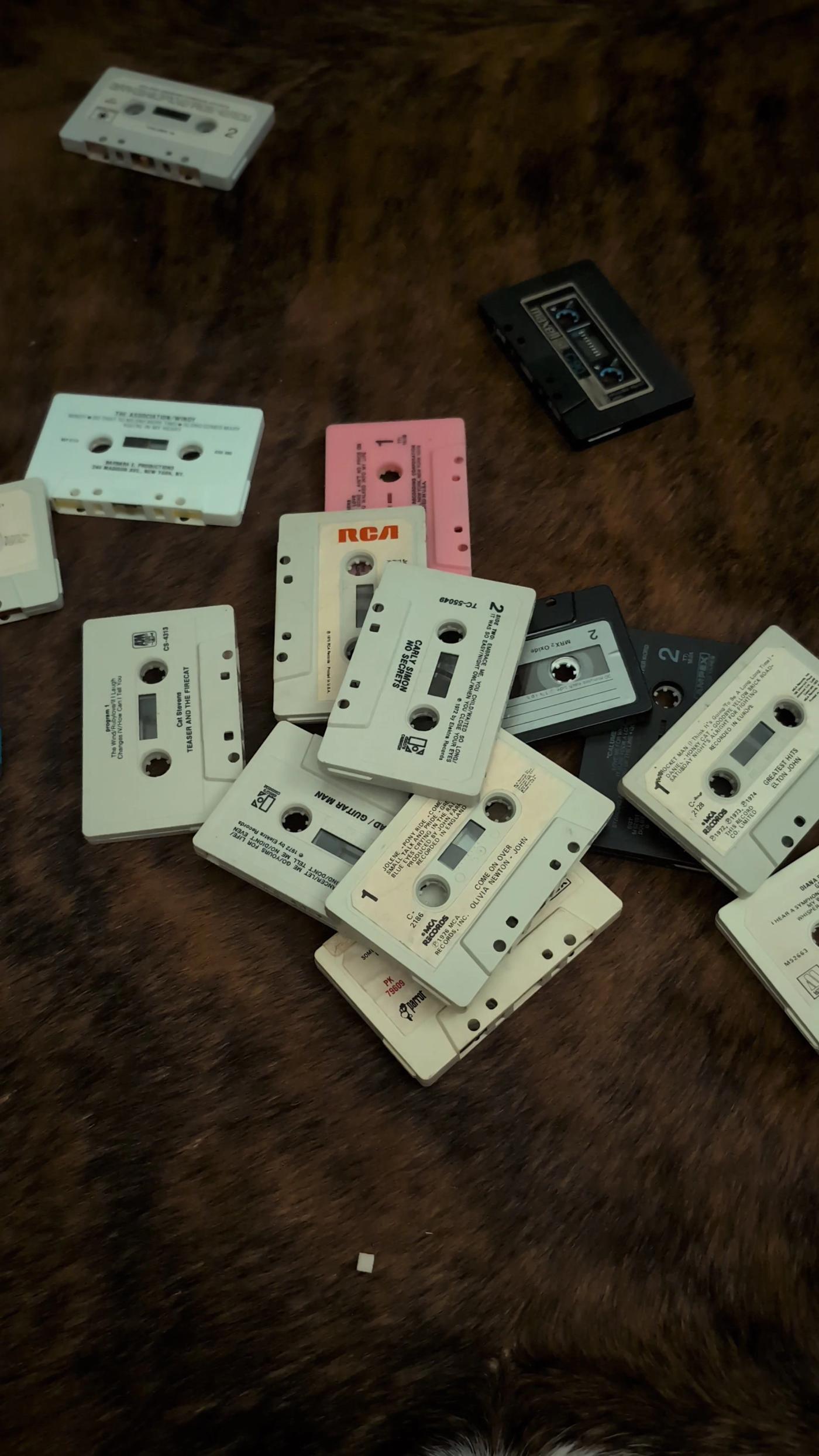 Loose vintage cassette tapes on a dark hide surface, with white, pink, grey and black shells plus original printed labels and side numbers