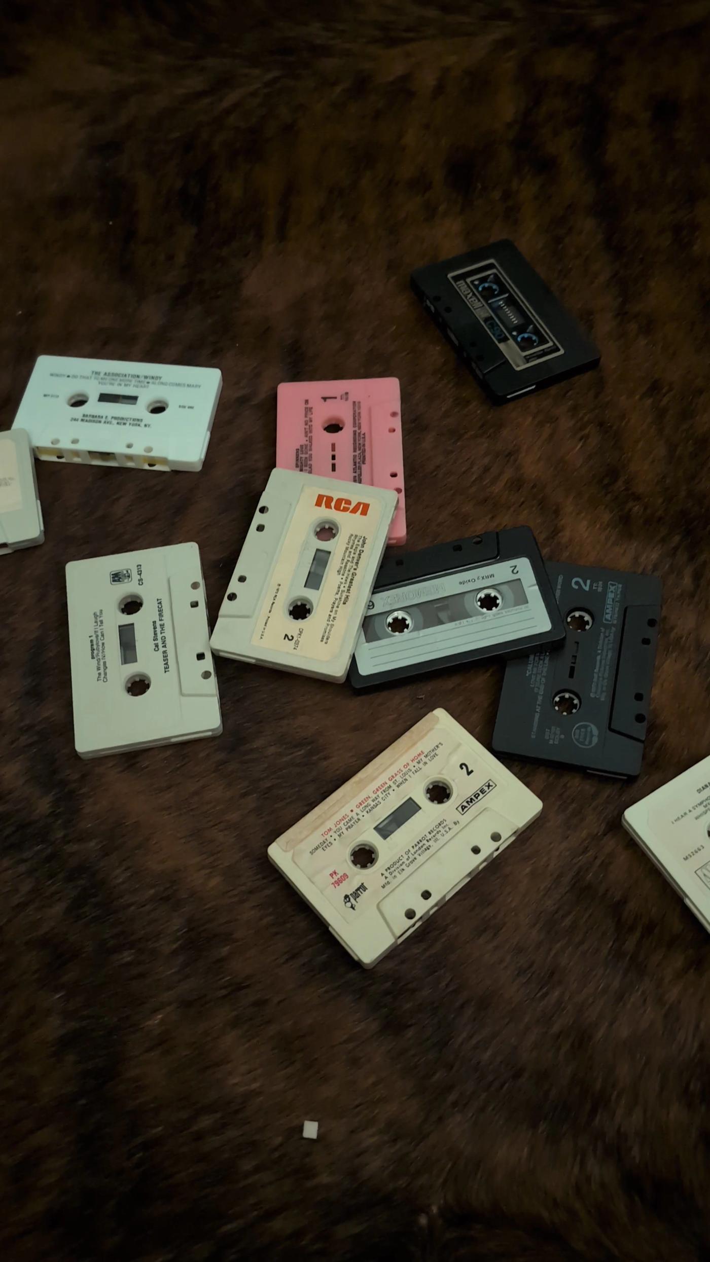 Loose vintage cassettes on a wooden surface, including an orange RCA label, a pink shell, and pale and dark cassette faces with original printed lettering
