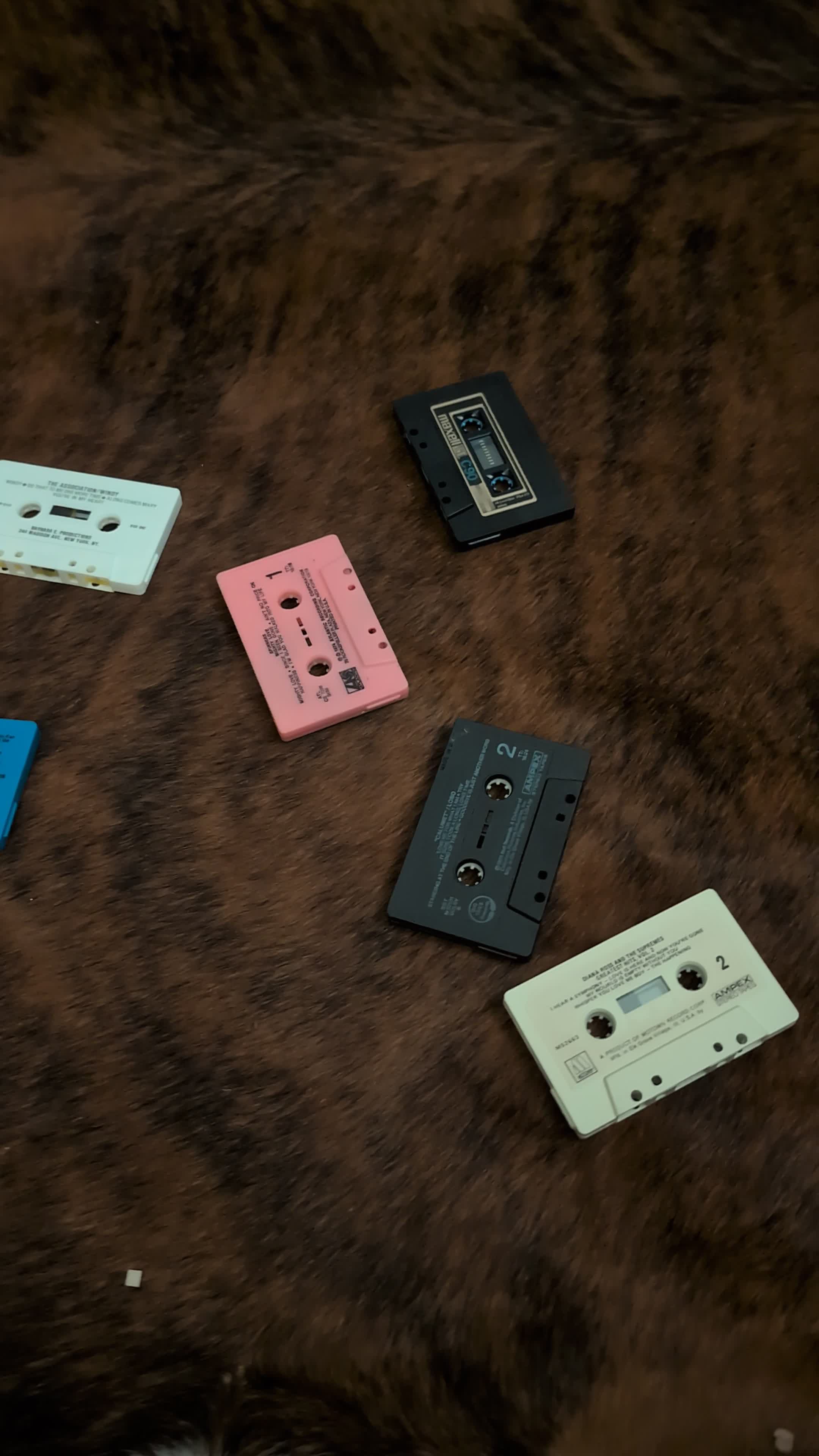 Loose white, pink, black, grey and blue vintage cassettes on a dark brown surface