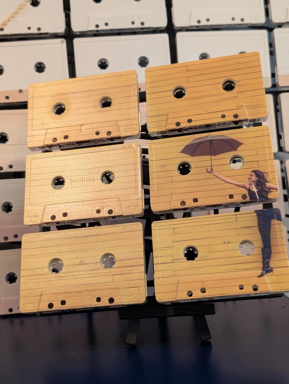 Small six-tape artwork with a figure holding an umbrella, displayed in front of a larger cassette grid