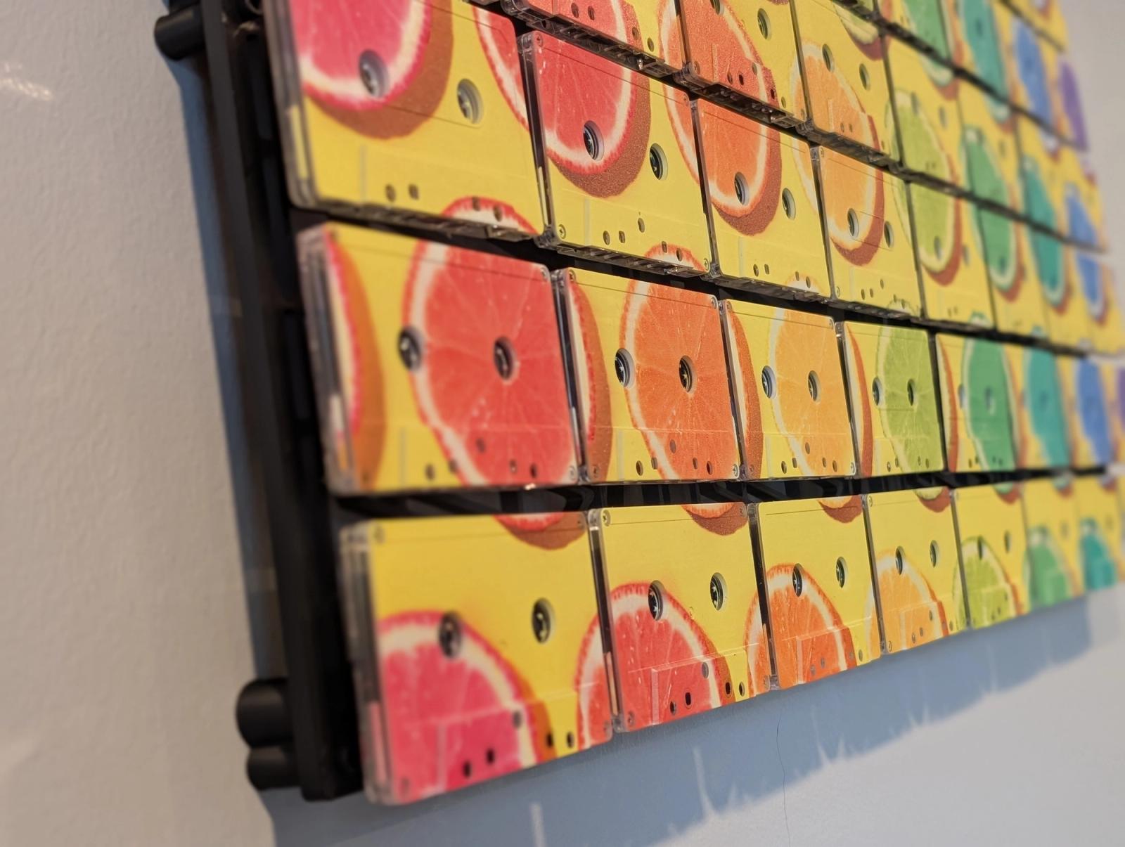 Angled close view of citrus artwork printed across cassette faces, with yellow and orange colour, reel openings, clear shell edges, and dark gaps