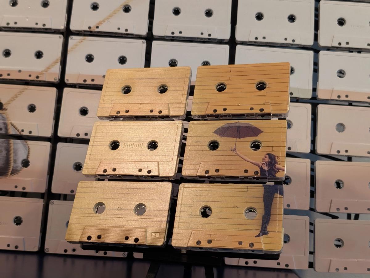 Six-tape artwork with pale lined cassette faces and a figure holding a dark umbrella on the right