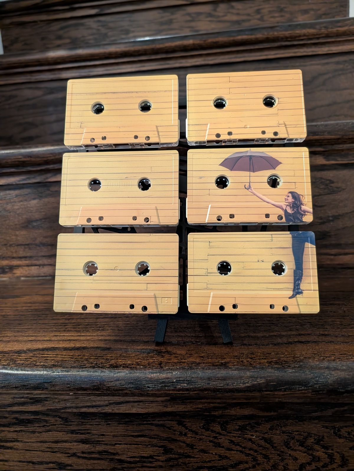 Front view of a six-tape umbrella-and-figure artwork against a dark wooden surface