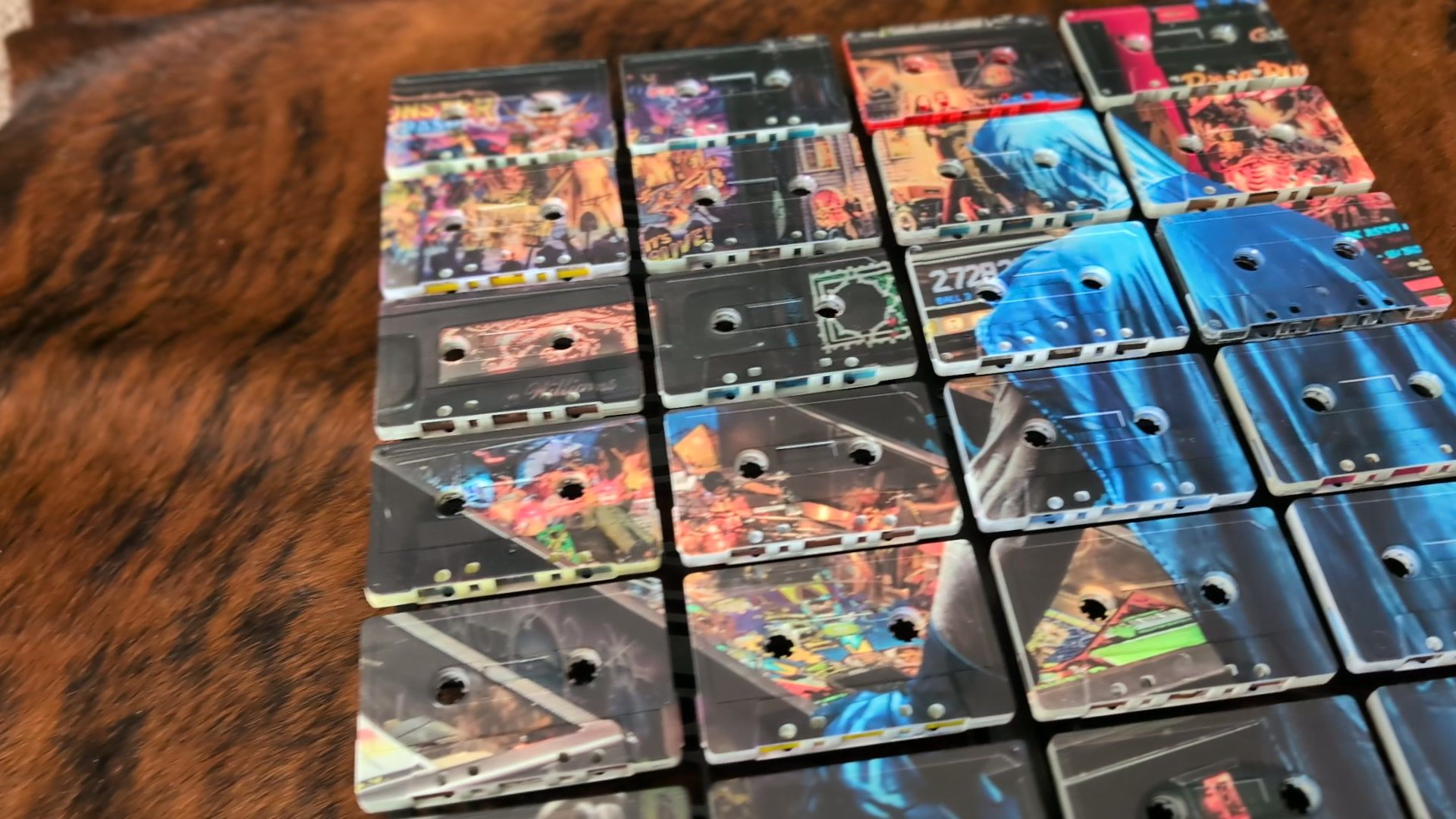 Angled close view of the blue cassette mosaic showing printed colour crossing cassette faces, circular reel openings, moulded shell outlines and gaps between rows.