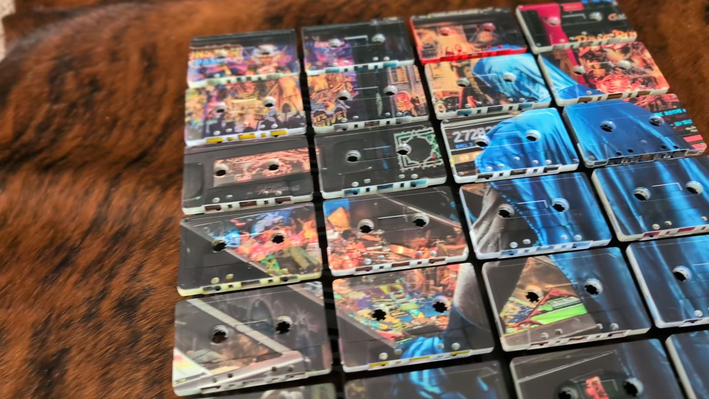 Angled close view of UV-printed cassette faces in a blue and multicolour 24-tape composition, showing reel openings, shell edges and label shapes