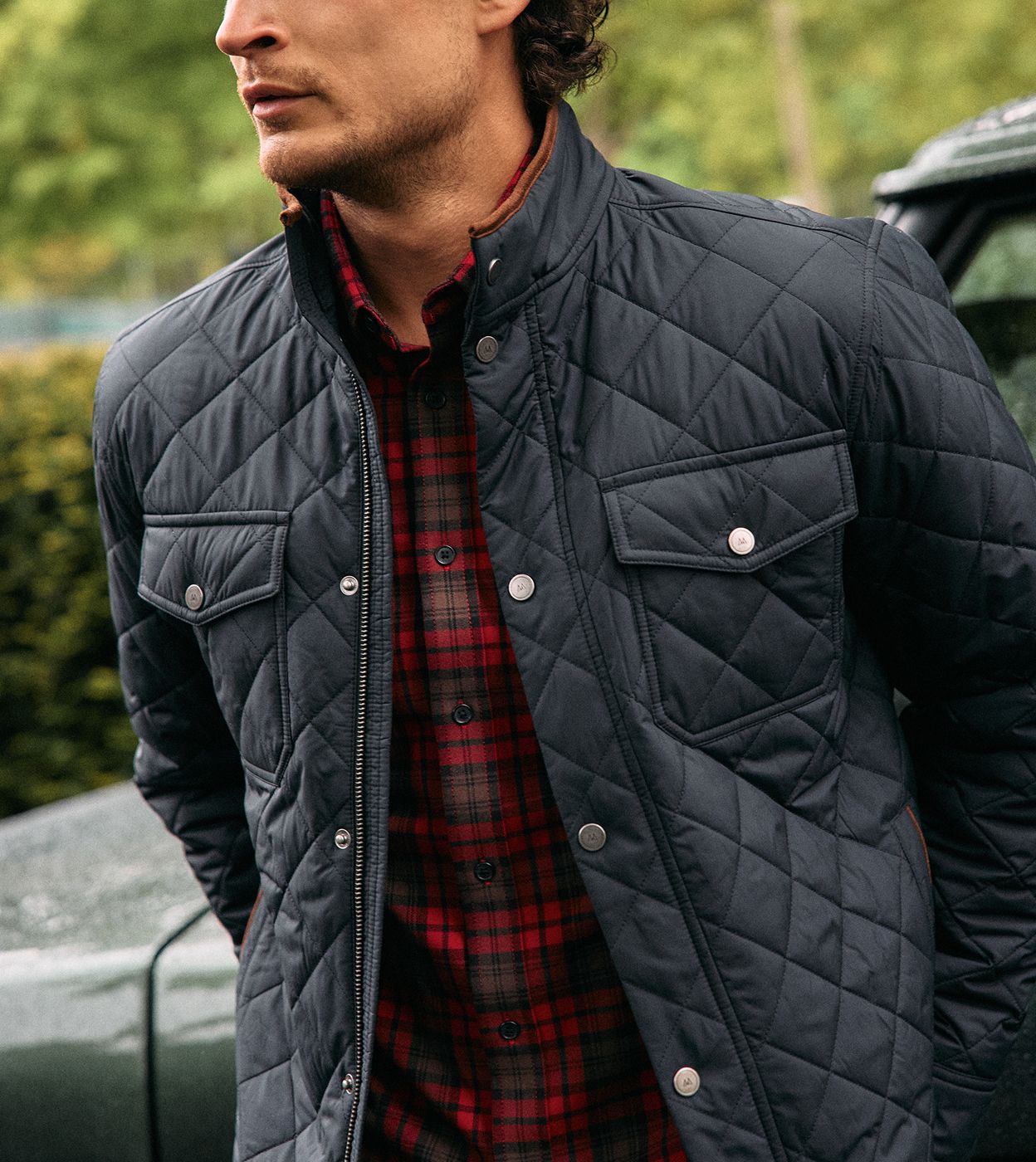 Close-up of a man wearing a navy quilted Brentwood Jacket over a red plaid shirt.