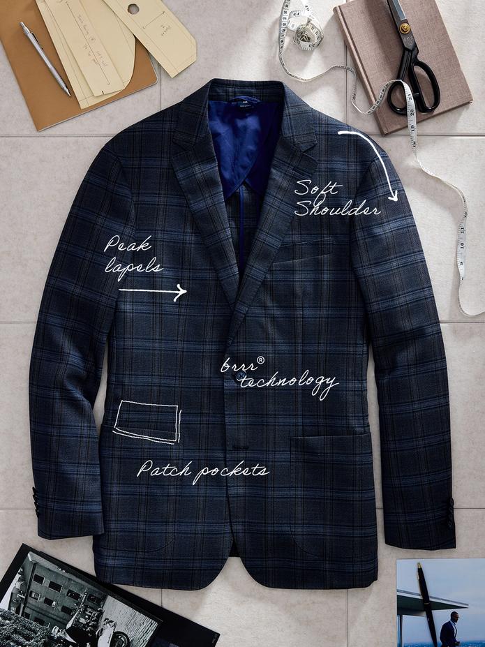 Product flat-lay of a dark blue plaid suit jacket with handwritten annotations identifying features like "Peak lapels", "Soft Shoulder", "brrr° technology", and "Patch pockets".