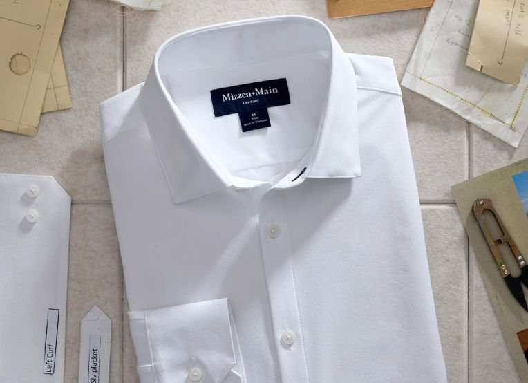 Folded white Mizzen+Main dress shirt laid flat among paper sewing patterns and thread snips