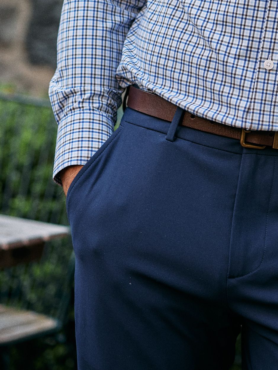 Close-up shot of a man's waist and pocket area wearing dark blue trousers, a brown leather belt, and a blue check shirt.