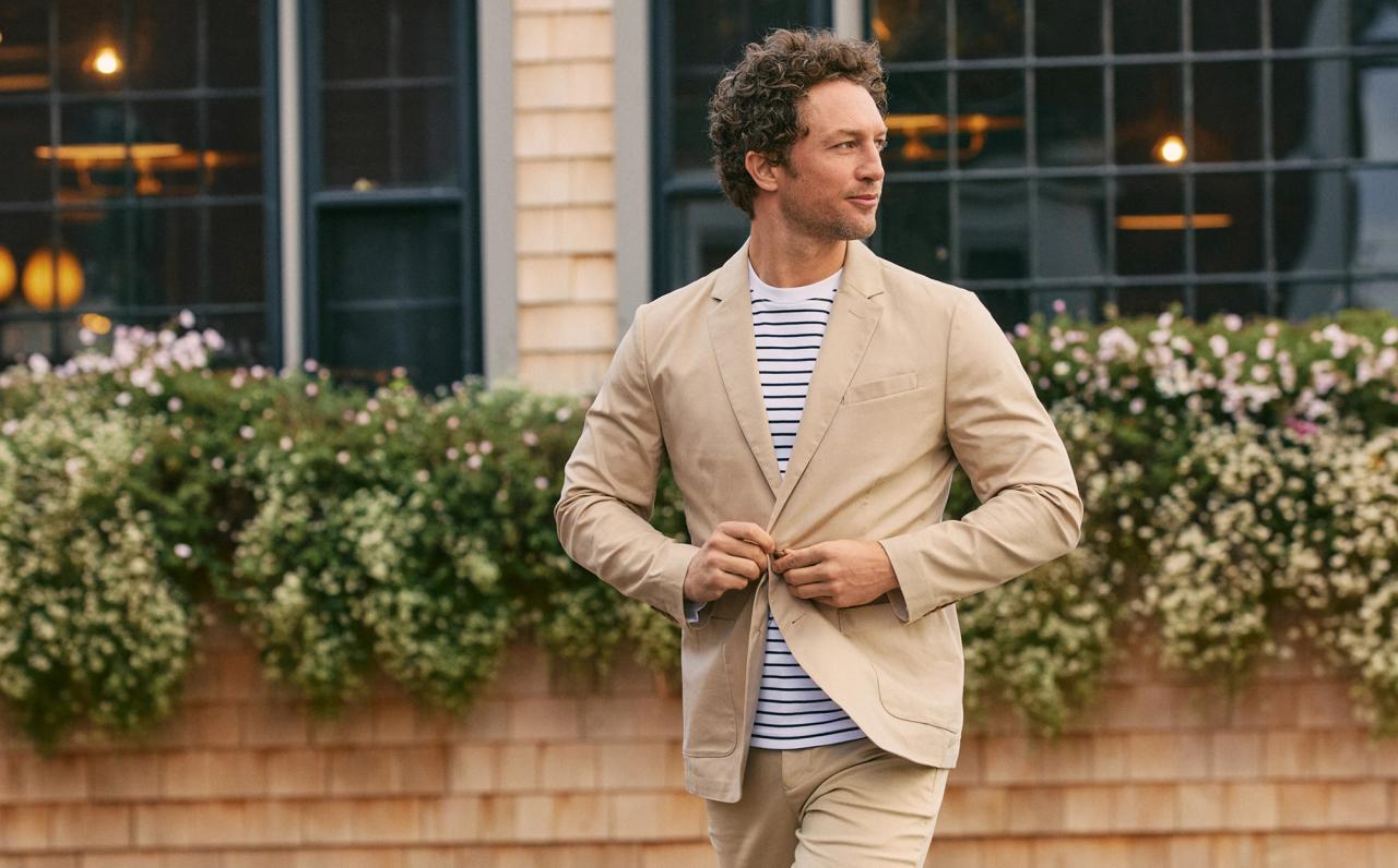 Man buttoning a tan Prescott blazer over a striped tee in front of flower boxes