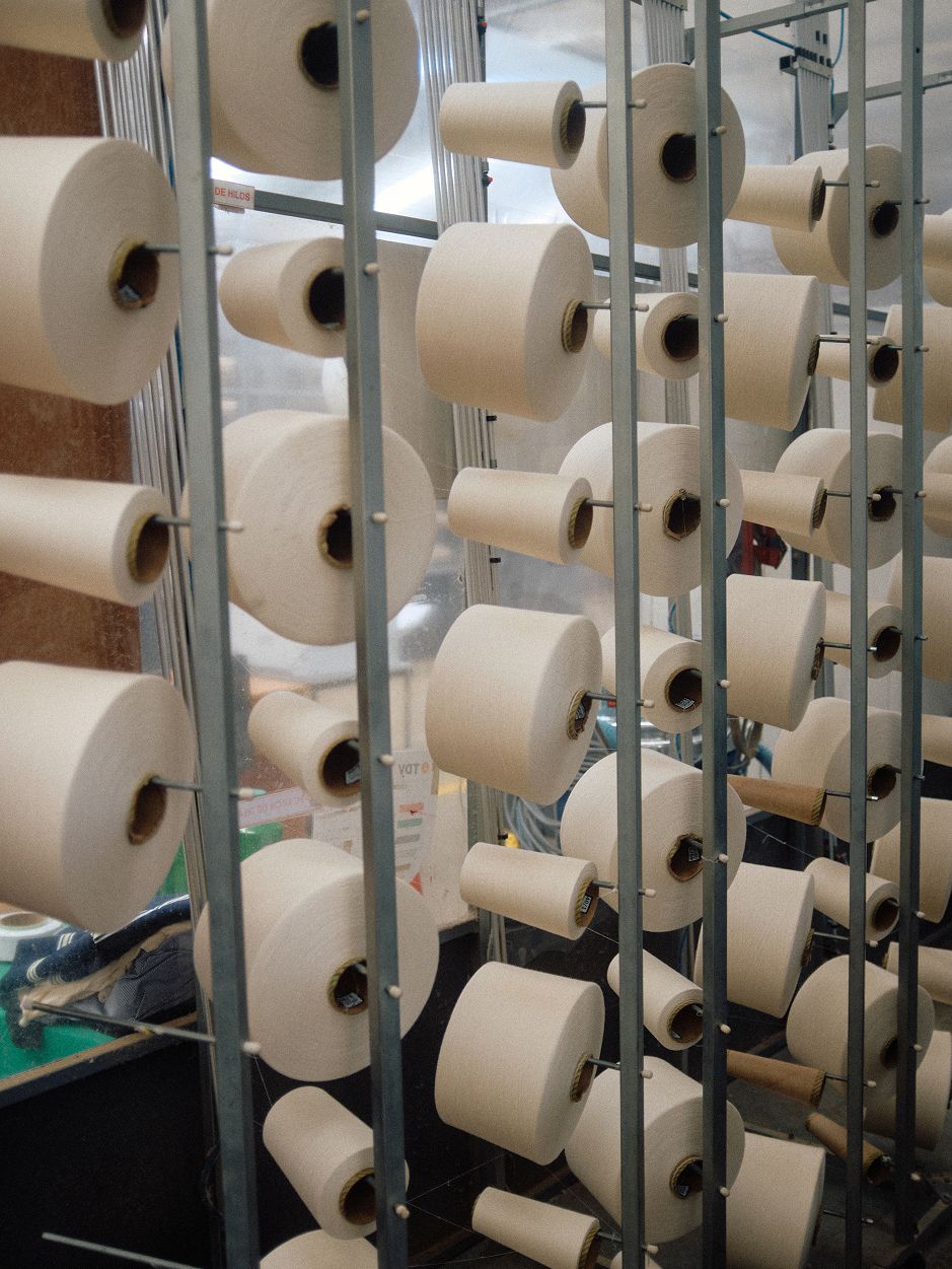 A full-color view of spools of white thread loaded onto industrial spools and creels in a textile factory.